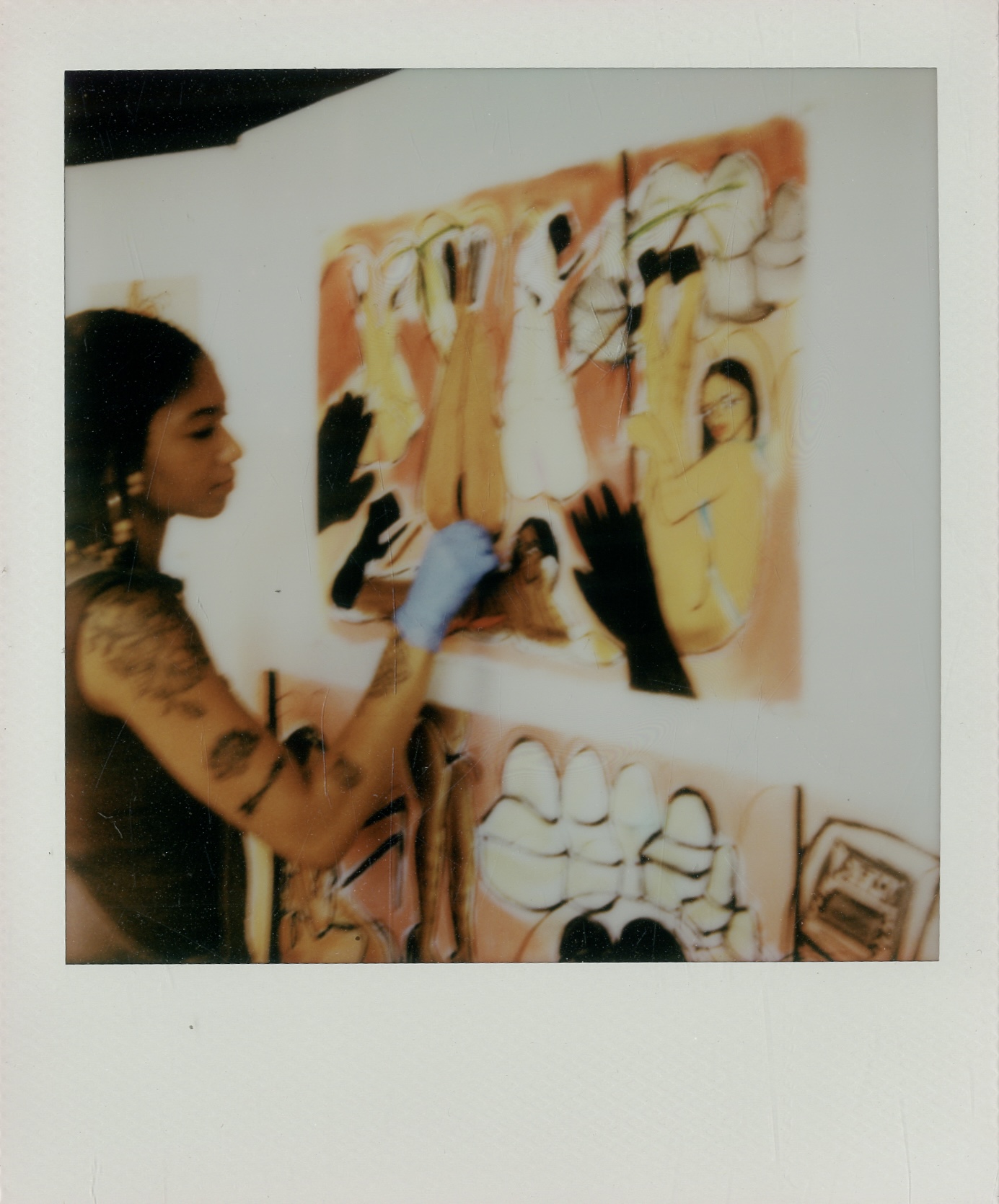 Young woman with dark hair and tattoos paints on a colorful canvas in an art studio.