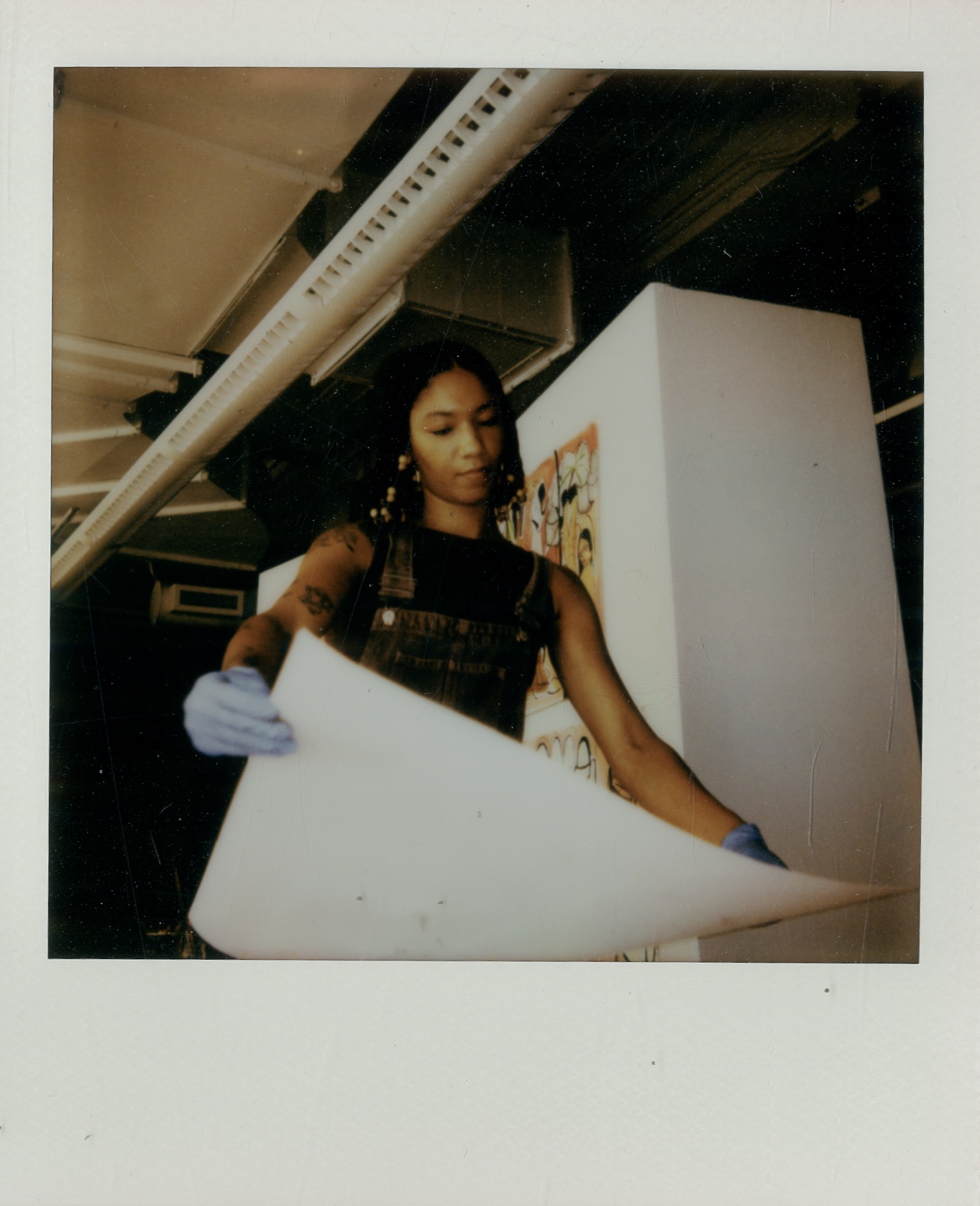 Woman examining artwork or documents in an indoor gallery or studio space, holding a large sheet of paper or canvas.