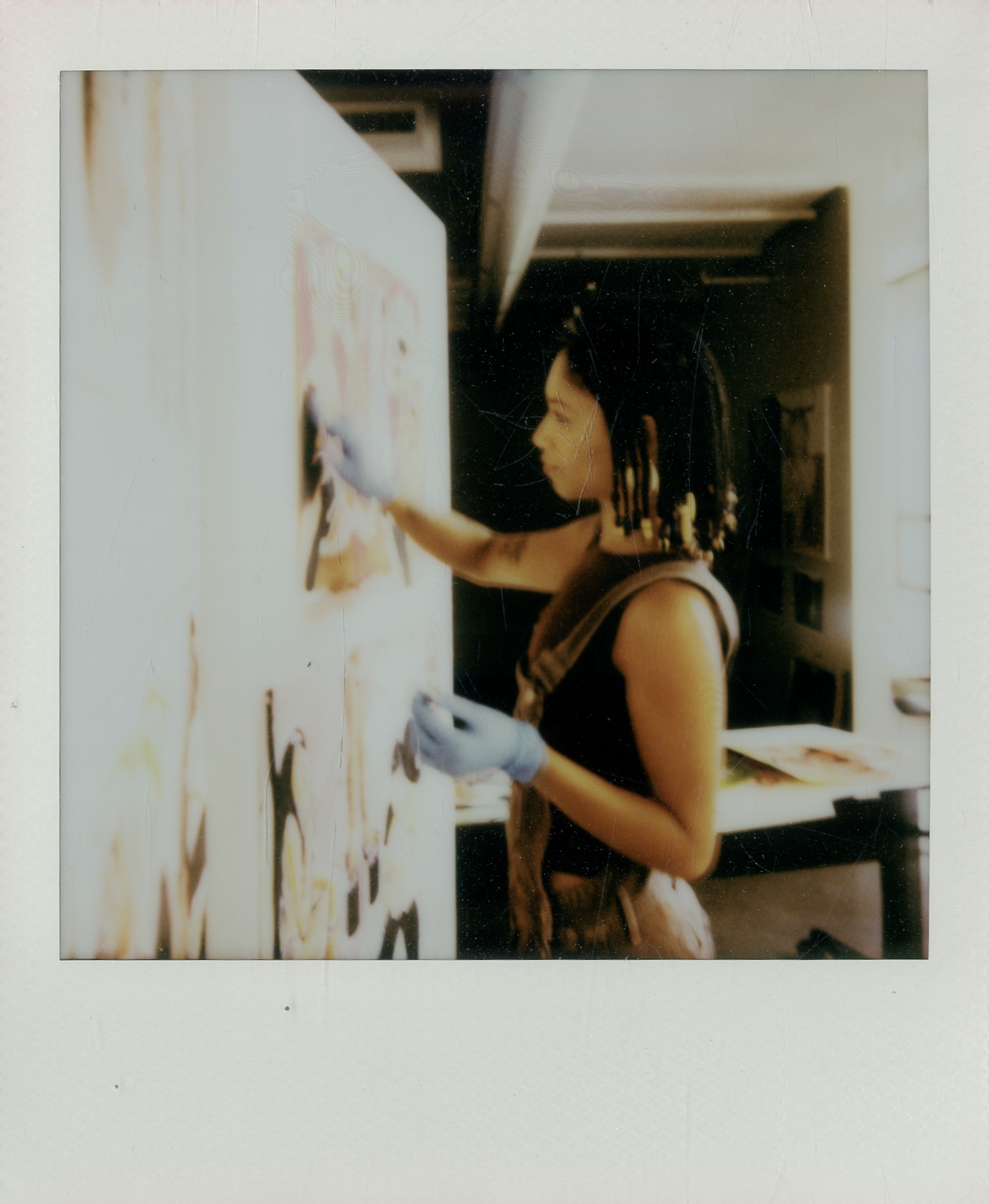 Person with dreadlocks wearing gloves, painting on a wall in an indoor space.