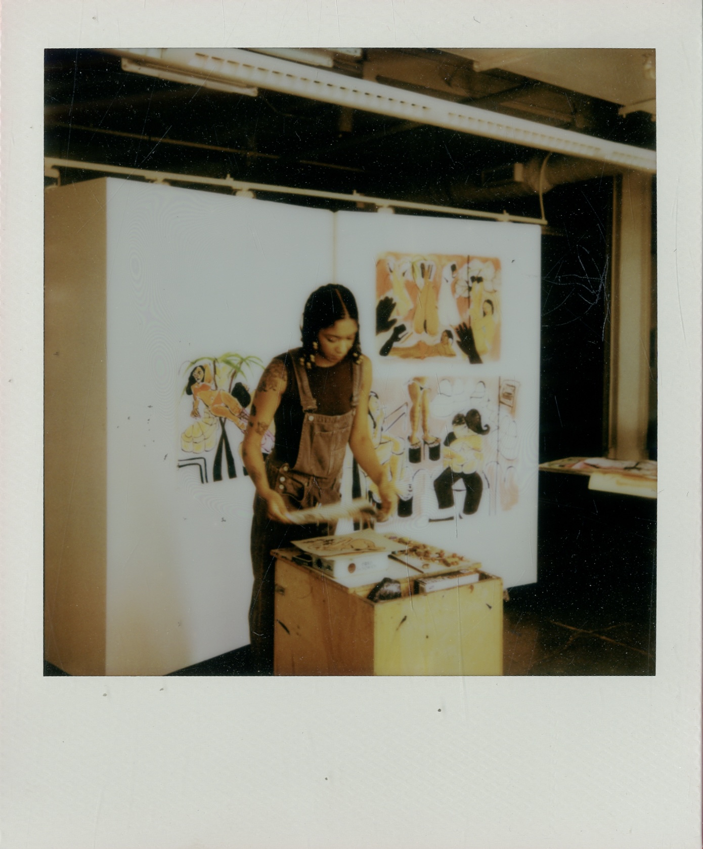 Person standing at an art display, looking at artwork on a white partition, with paintings behind them, in an indoor setting.