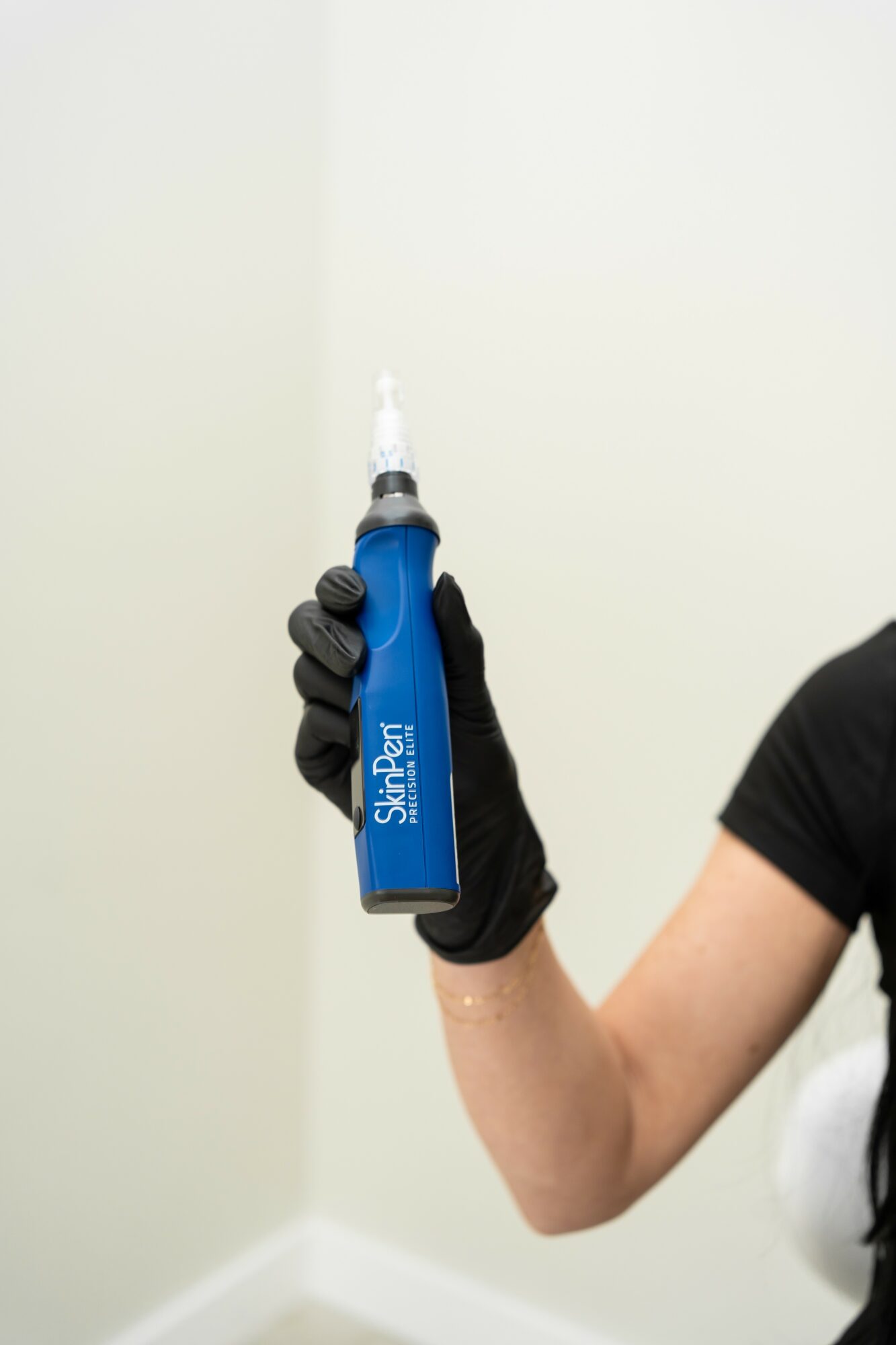 Person wearing black glove holding a blue and white dental syringe against a plain wall.