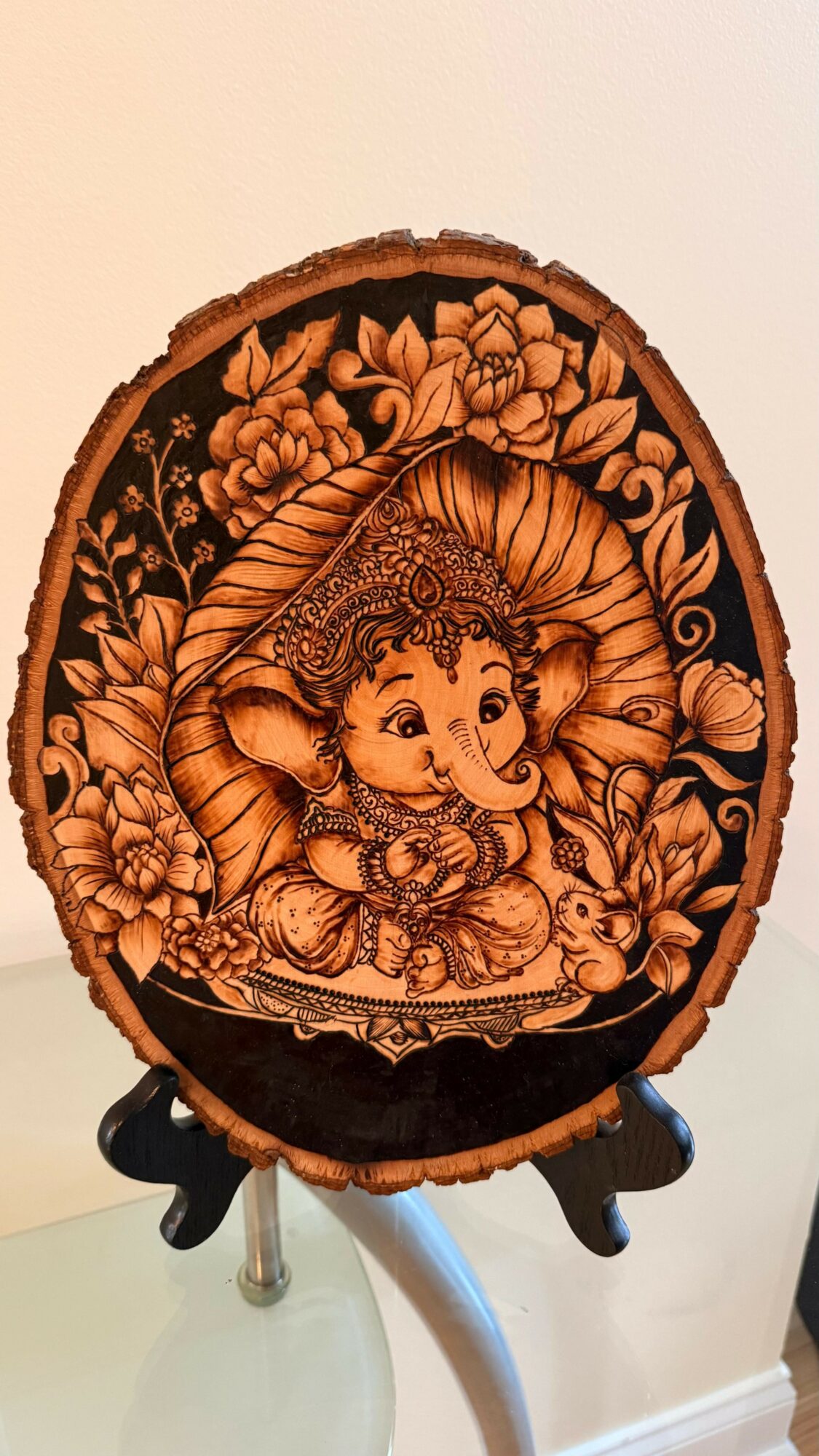 Wooden carving of Lord Ganesha with floral details, displayed on a stand.