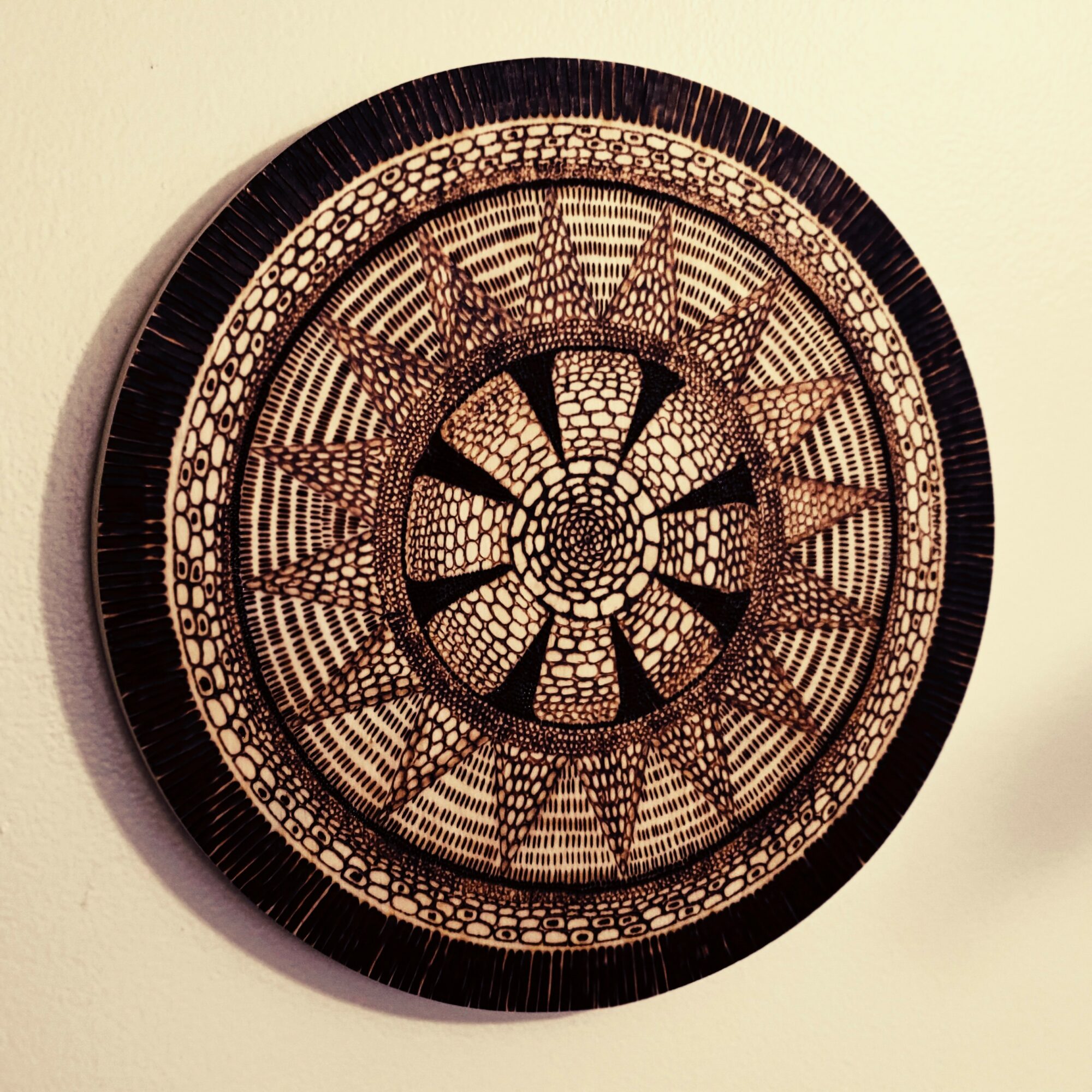 Decorative circular woven basket with intricate patterns, black and beige colors, hanging on a wall.