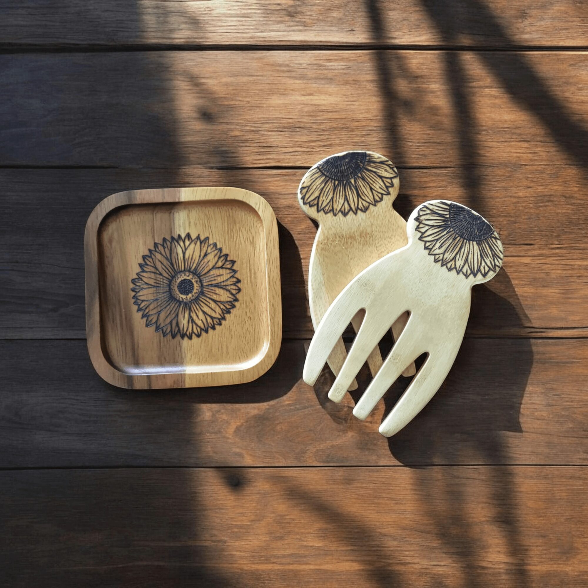 Wooden dish and two wooden utensils with floral designs on a wooden surface, sunlight and shadows present.