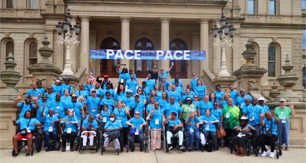 Group of people wearing blue shirts gathered in front of a historic building with columns and statues, holding a banner that says 'PACE'.