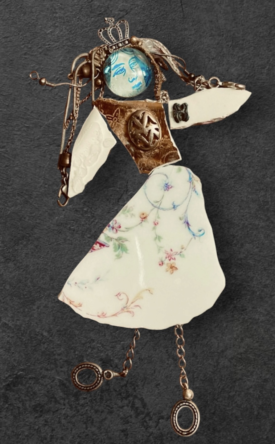 Decorative doll with a blue face, gold crown, white dress, and metal chain limbs, on a dark background.