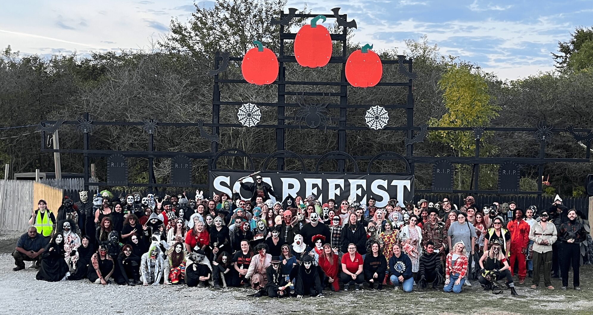 Large group of people gathered outdoors in front of a stage with a sign reading 'SCARE FEST' and hanging red lanterns.