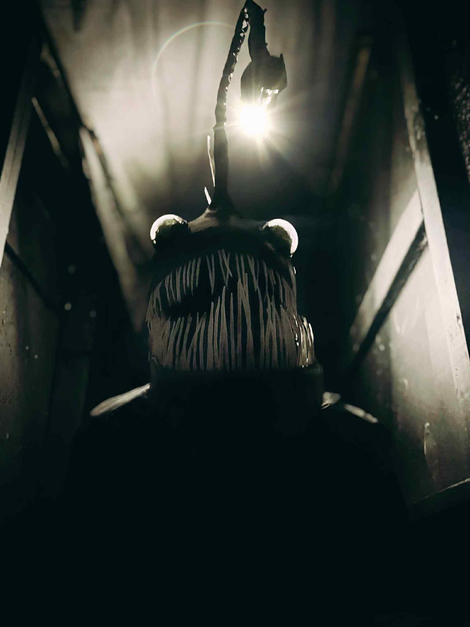 A person hanging upside down with a rope, backlit by a bright light, in a narrow space with walls on sides.
