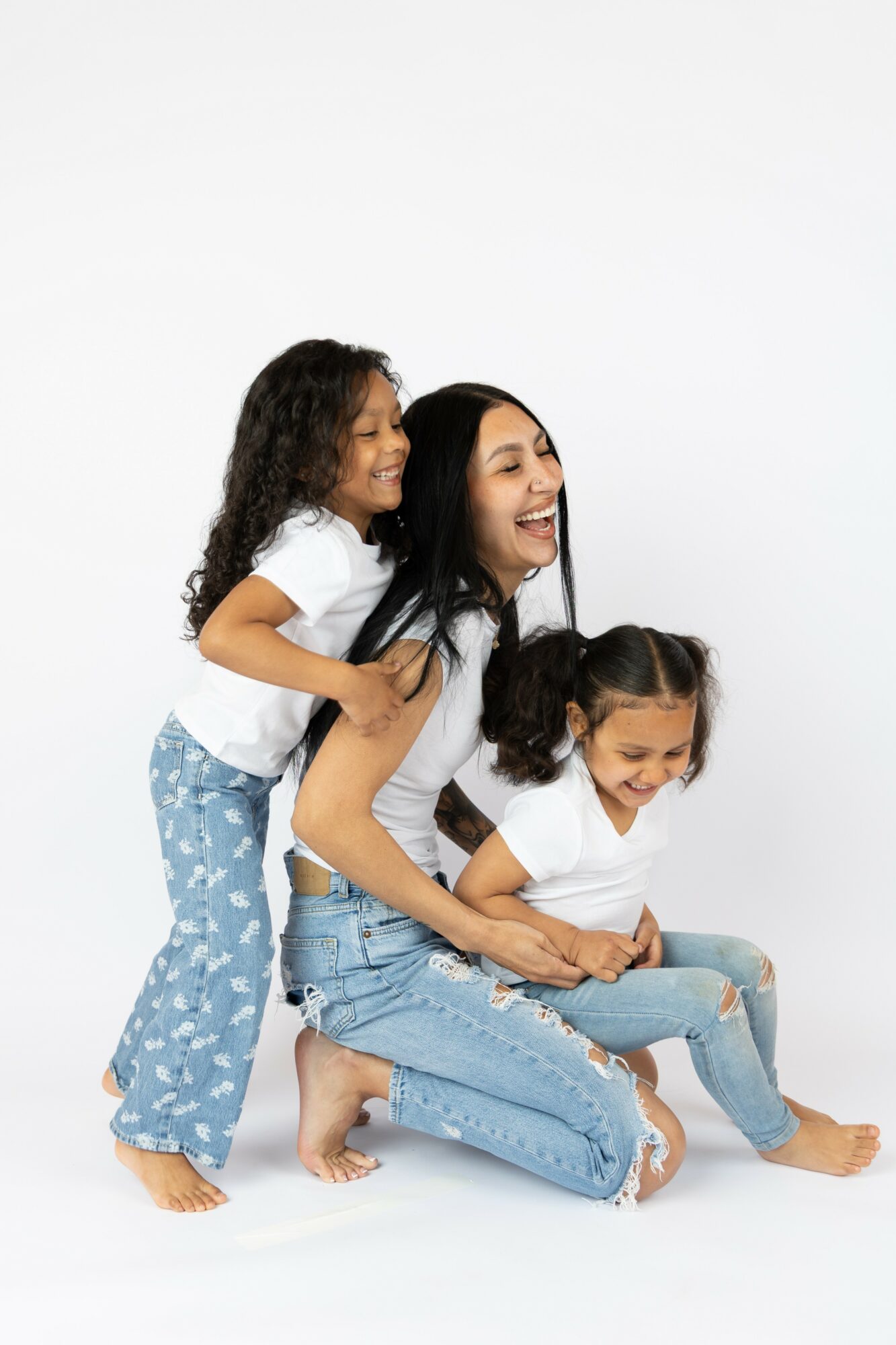 Woman and two children playing together, smiling, sitting on the floor against a white background.