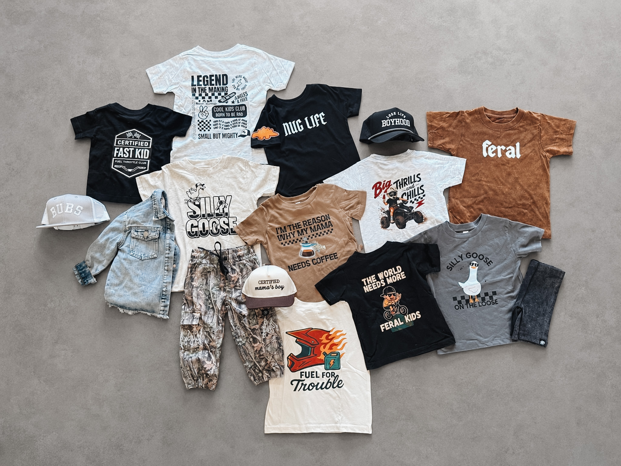 Collection of children's T-shirts, pants, and hats arranged on a gray surface, with various colors and designs.