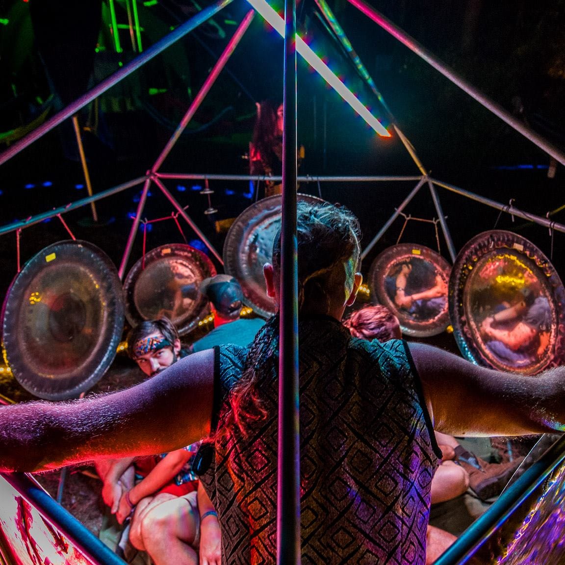 Person with arms outstretched surrounded by circular reflective objects and colorful laser lights at a party or event.