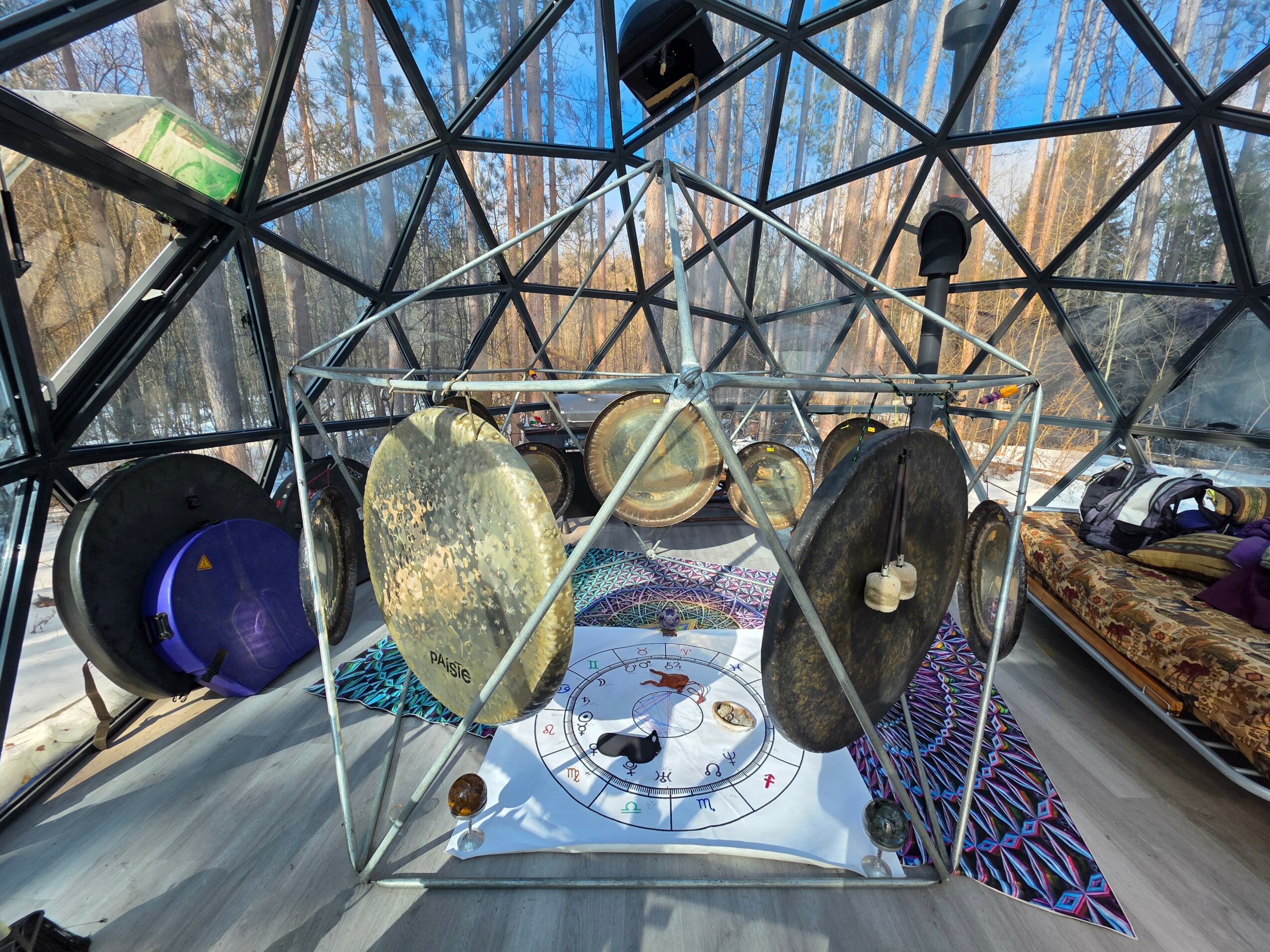 Interior of a geodesic dome with musical instruments and a decorative floor, surrounded by trees outside.