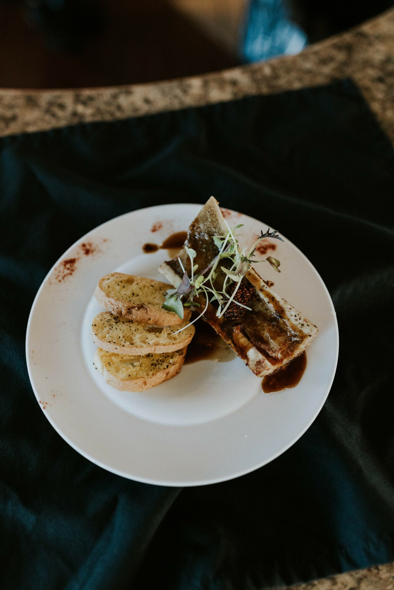Three small sandwiches and a piece of chocolate cake on a white plate, garnished with microgreens.