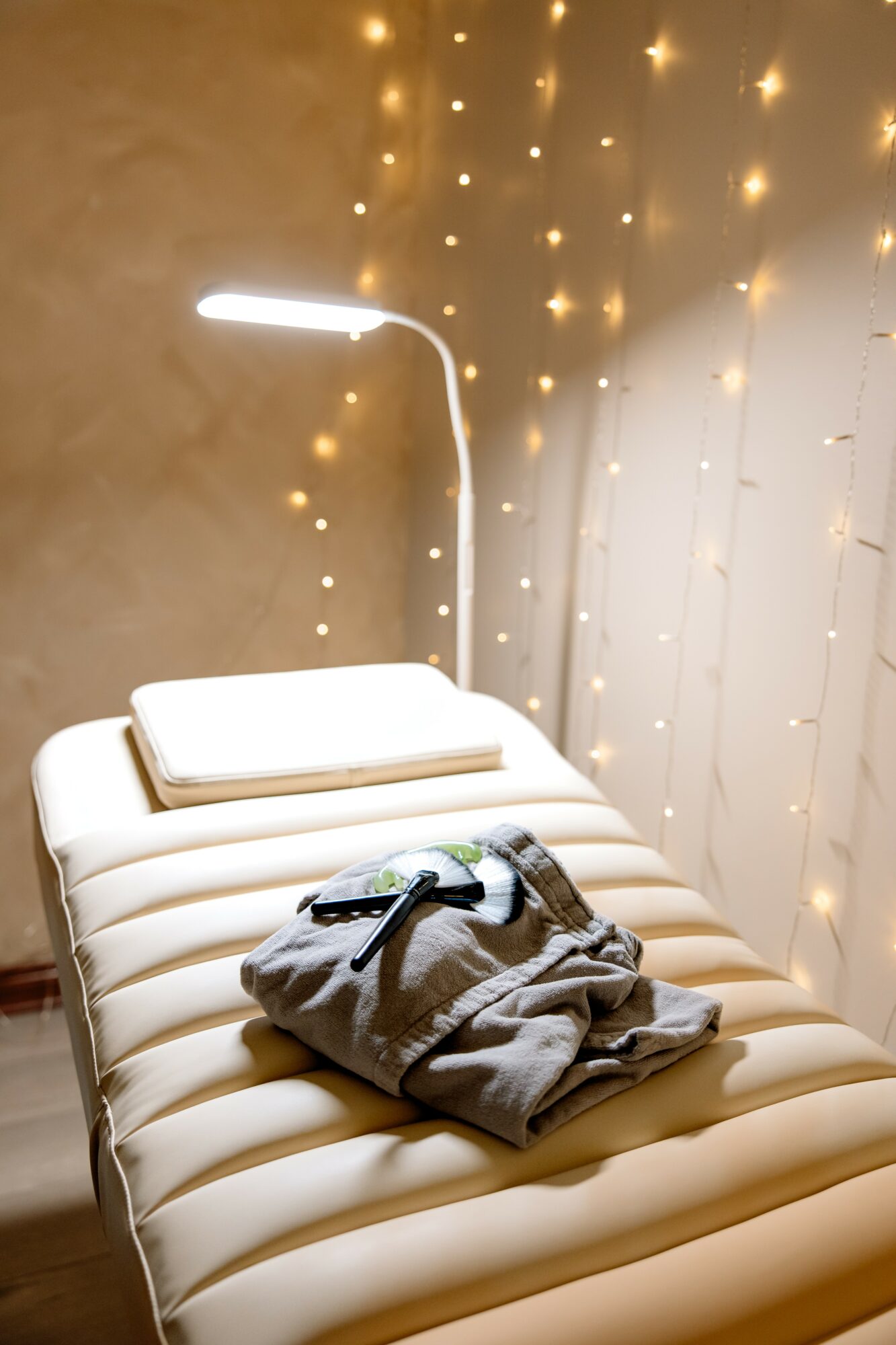 Bed with pillows and clothes, illuminated by a curved lamp, against a wall with string lights.