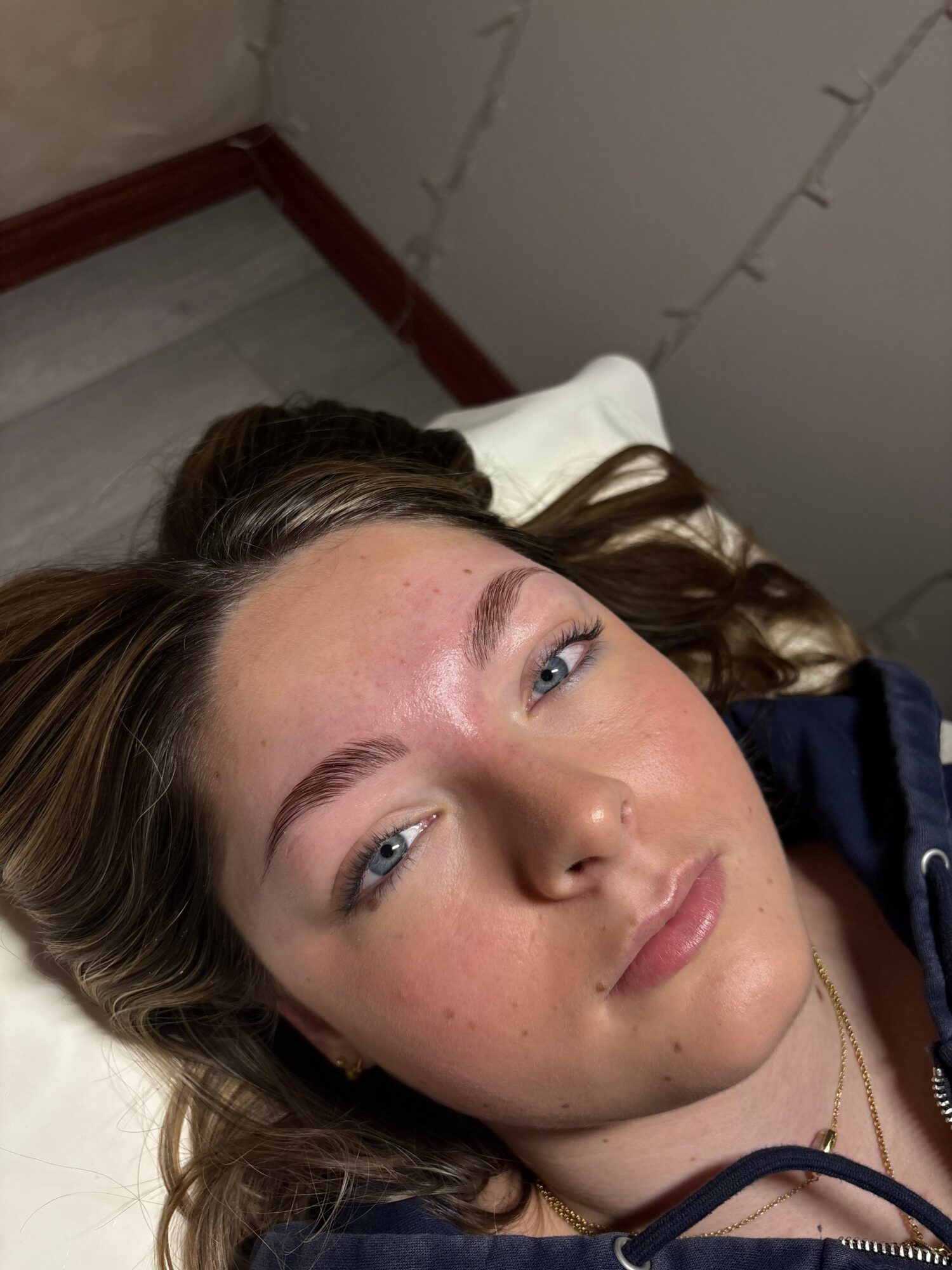 Young woman with light skin and blue eyes lying on a pillow, looking at the camera, with a neutral expression.