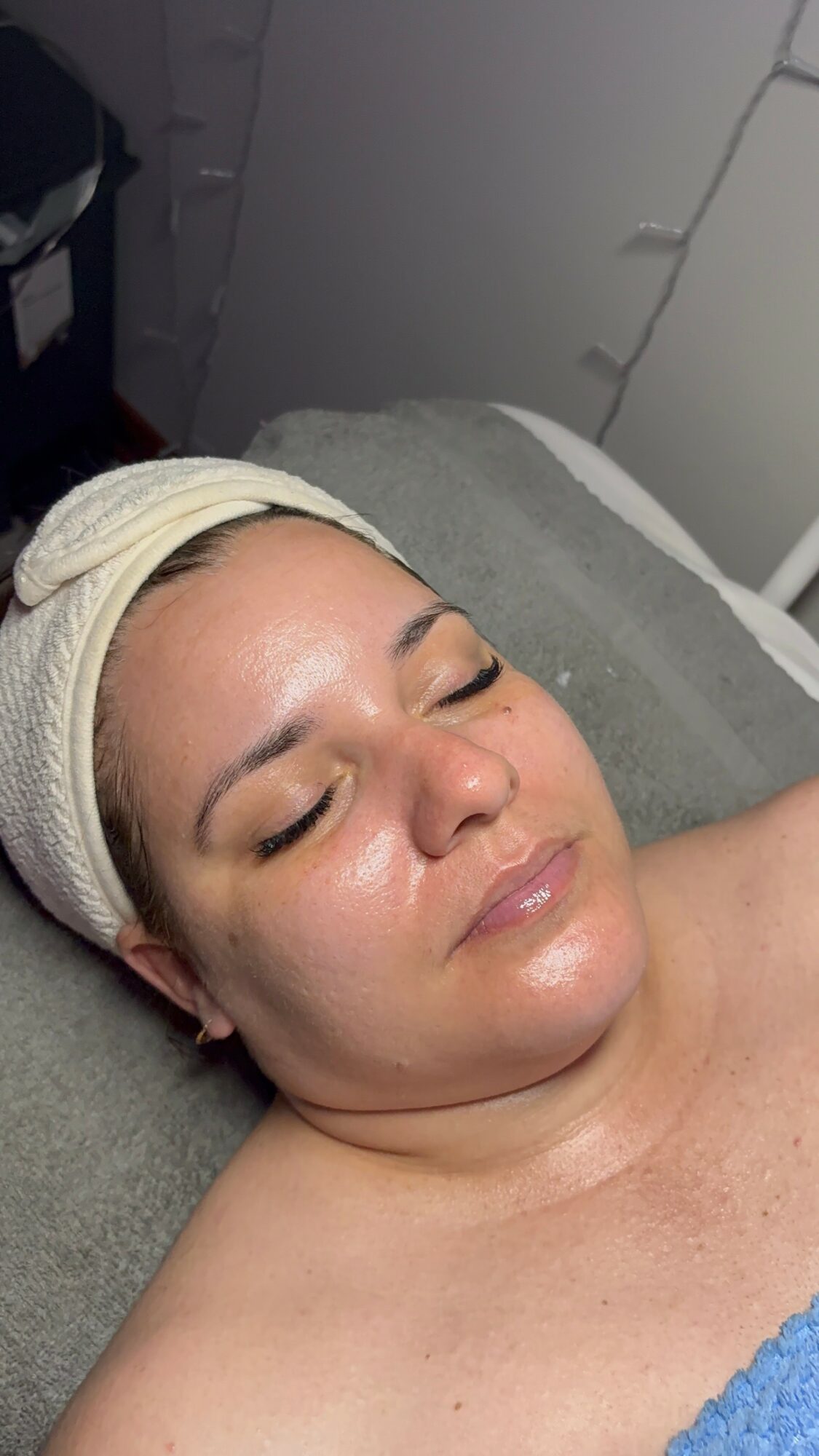 Woman with a headband lying on a bed with eyes closed, relaxed expression, in a room with white walls.