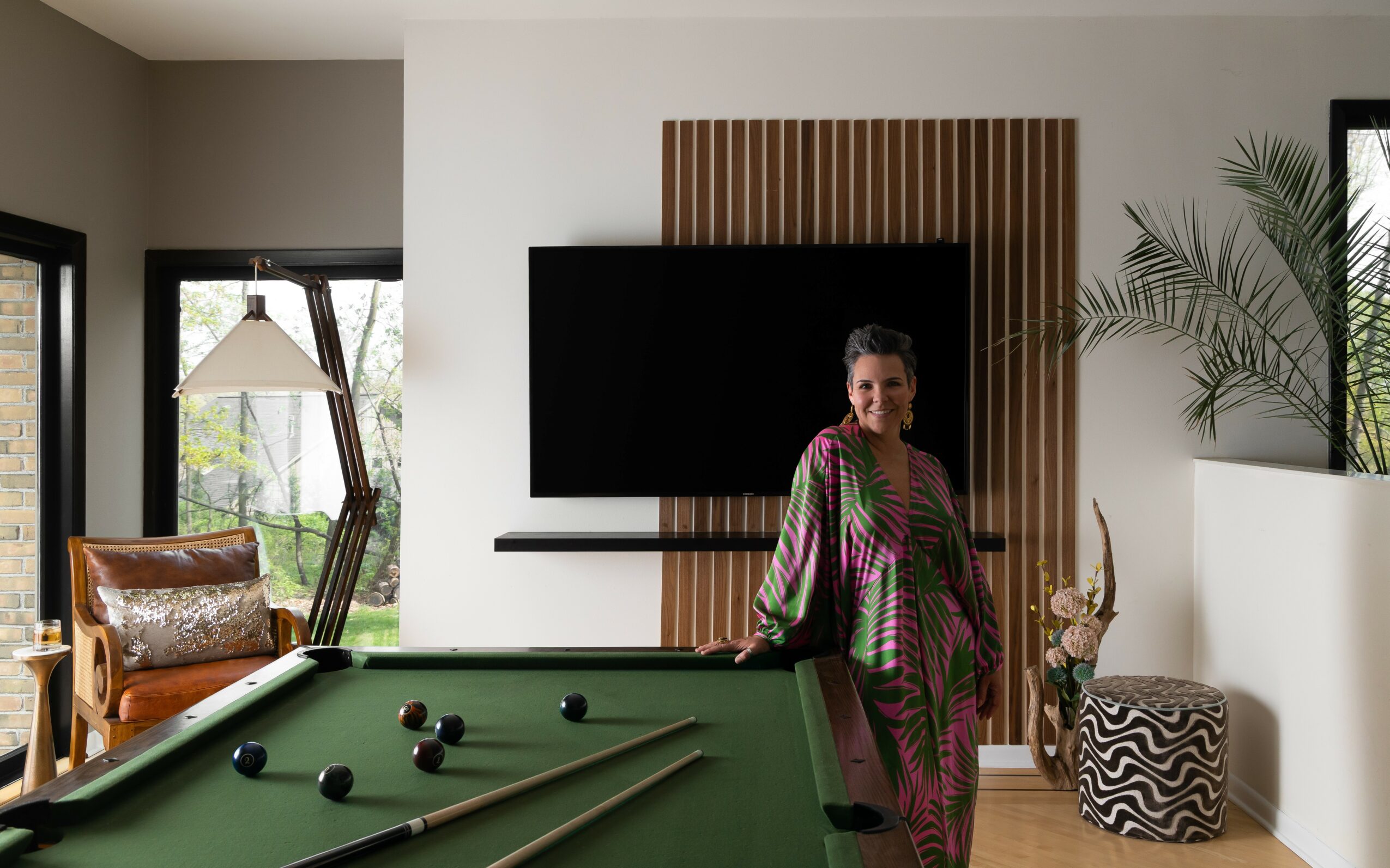 Woman standing near a green pool table in a modern living room with a wall-mounted TV and large window.