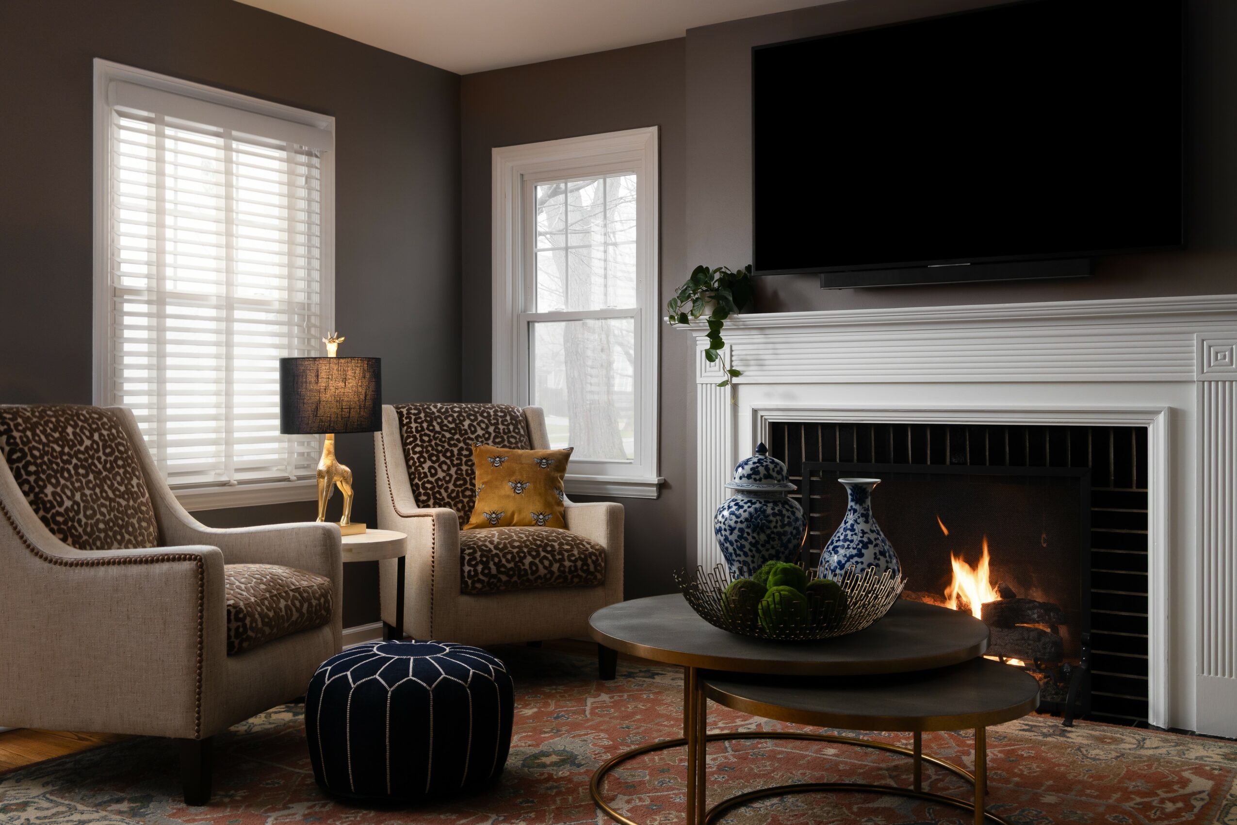 Living room with two armchairs, a coffee table with decorative vases, a fireplace, and a large TV above the mantel.