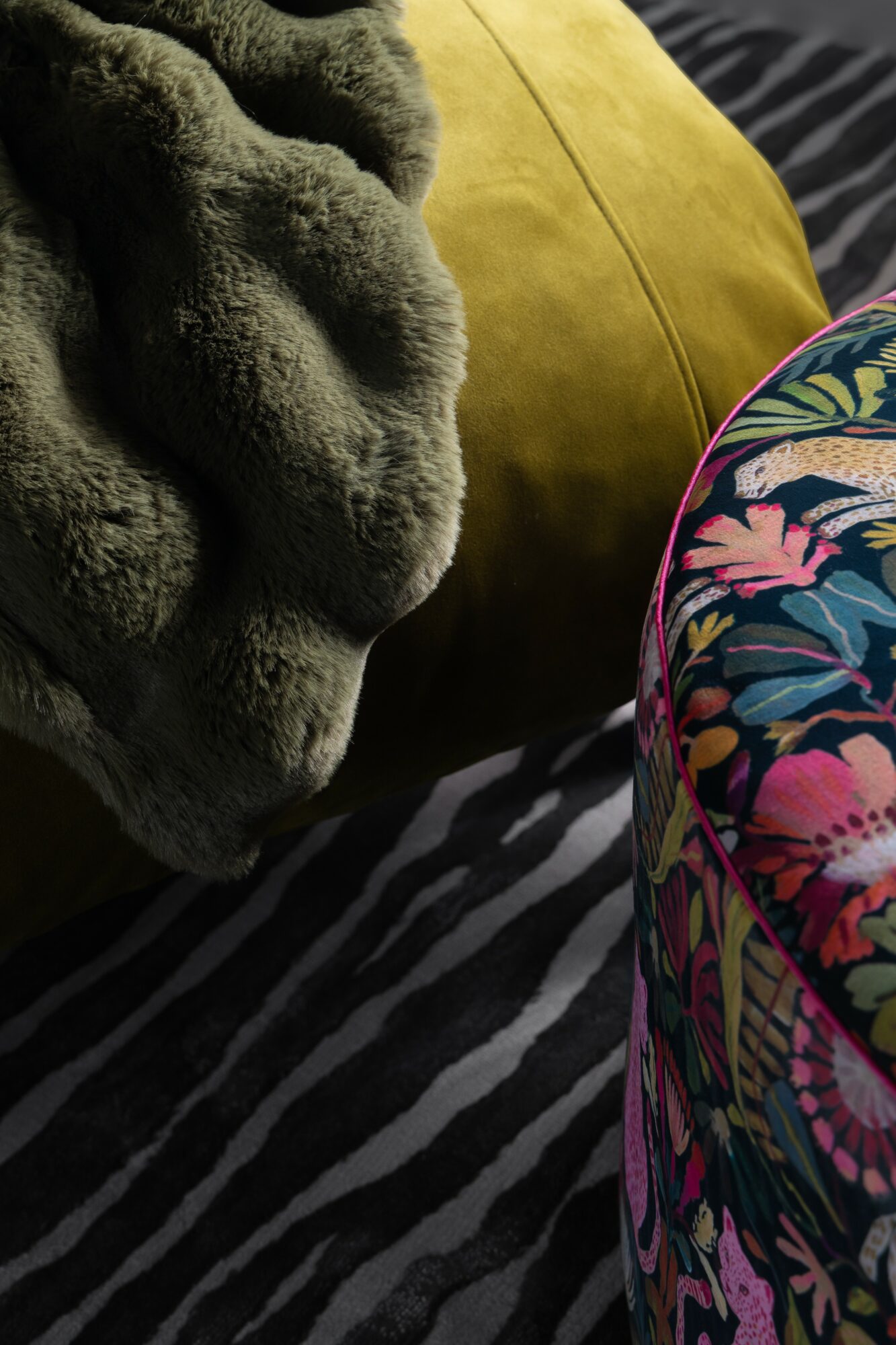Close-up of a plush gray blanket, a yellow pillow, and a colorful floral-patterned bag on a striped fabric surface.
