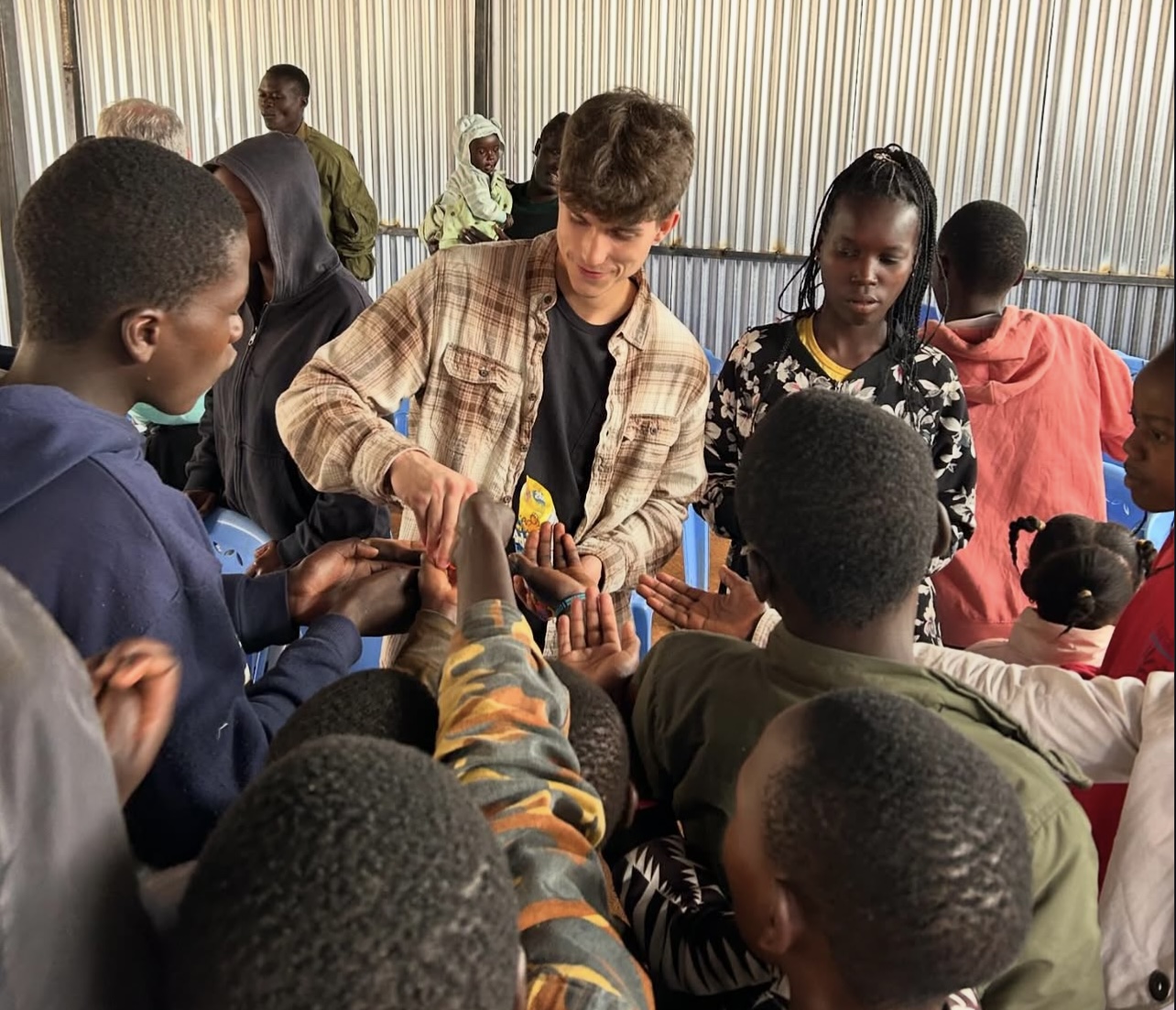 Group of children and a young man exchanging items indoors, with a striped curtain background.