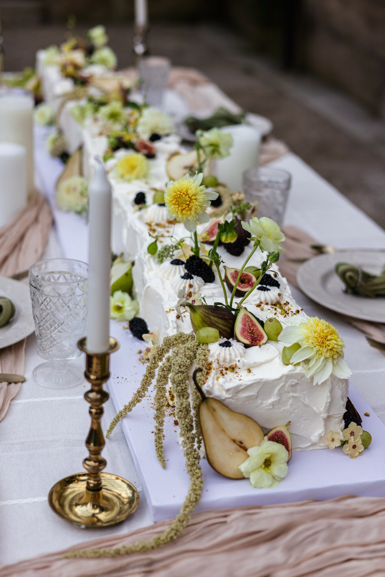 Decorated table with white cakes, flowers, candles, and tableware for celebration, with a blurred outdoor background.