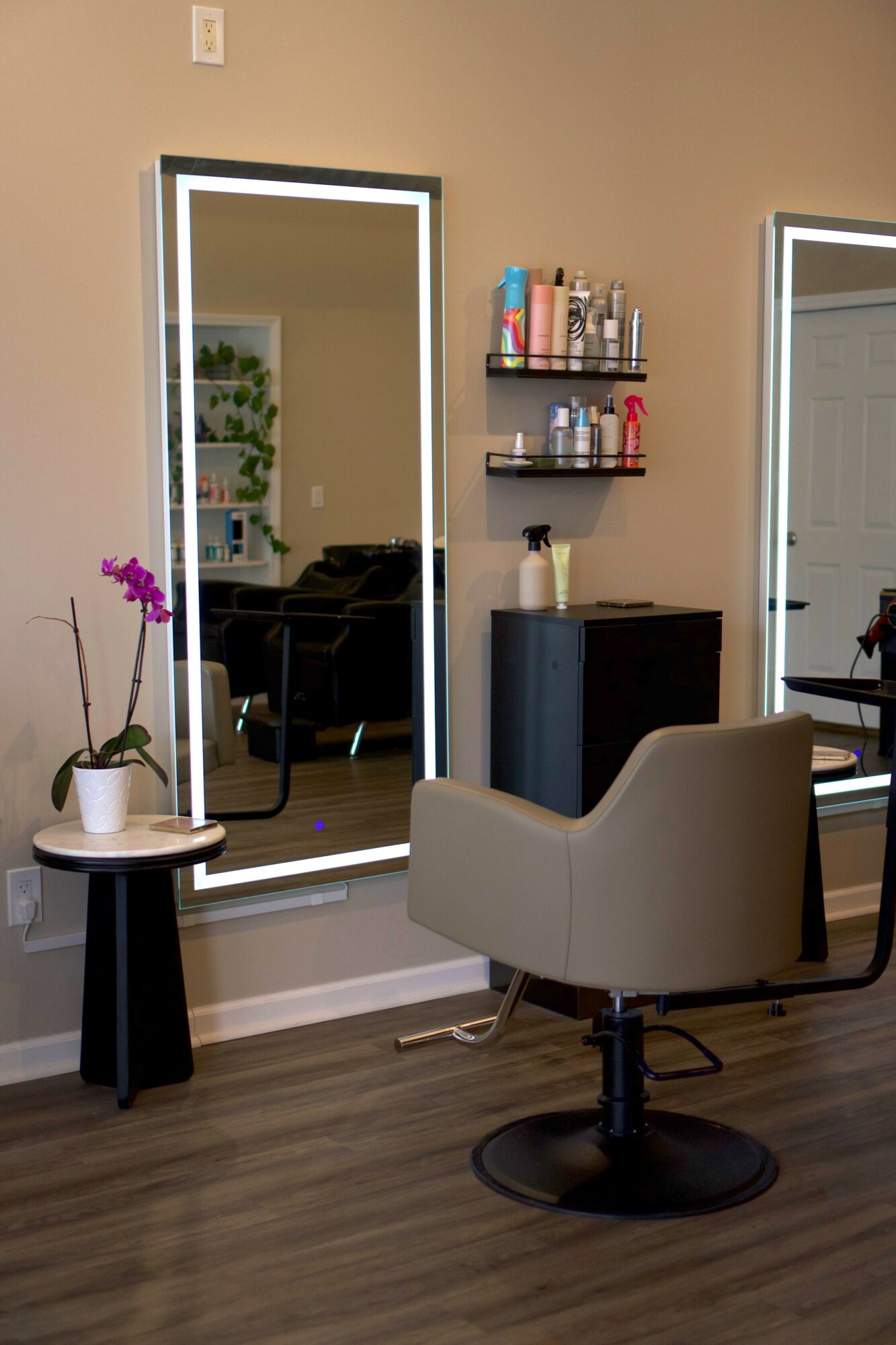 Office space with a white chair, black table, and a large mirror reflecting a plant and window.