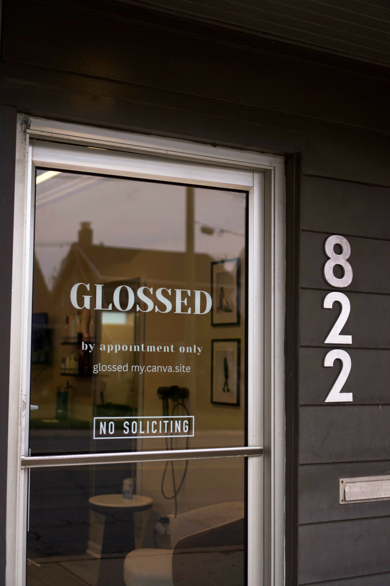 Glass door with a sign reading 'CLOSED' and a no soliciting sticker, reflecting a building and sky outside.