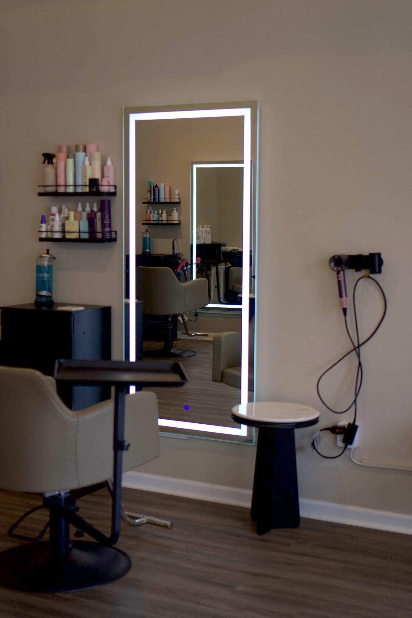 A room with a mirror, a chair, a small table, and a bookshelf with books, viewed from the side.