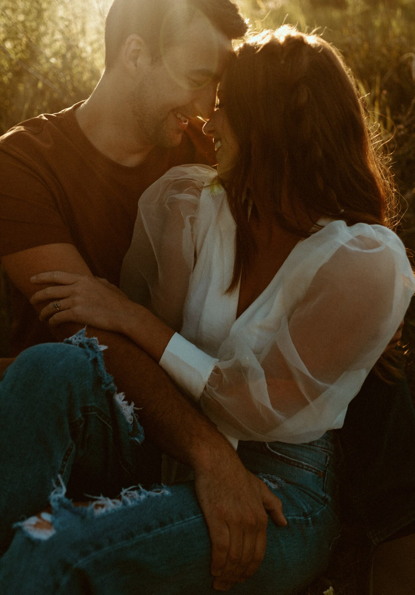 A man and woman face each other outdoors during sunset, smiling and close together, with sunlight behind them.