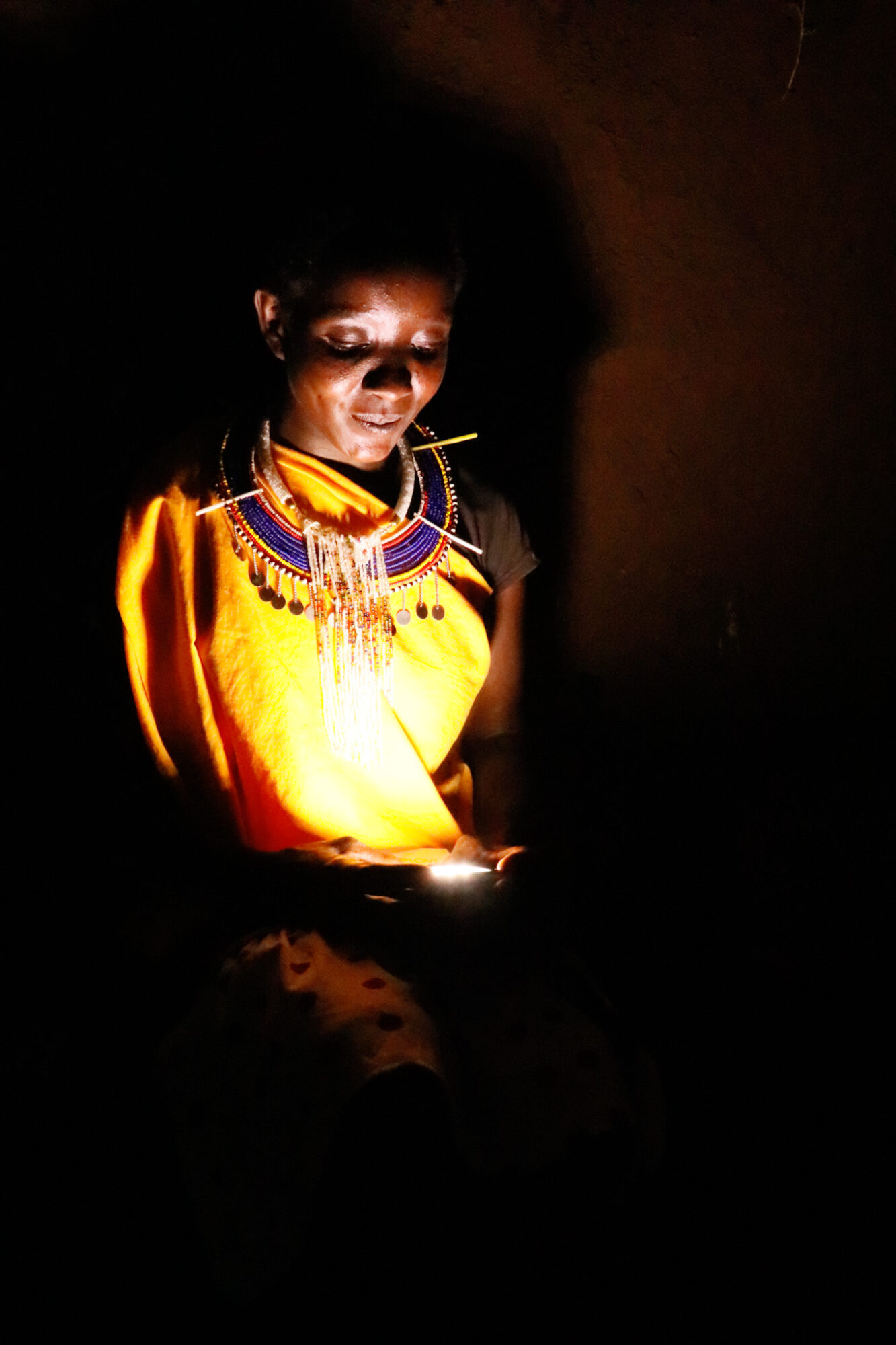 Person wearing traditional jewelry and clothing, illuminated by a light source, with a dark background.