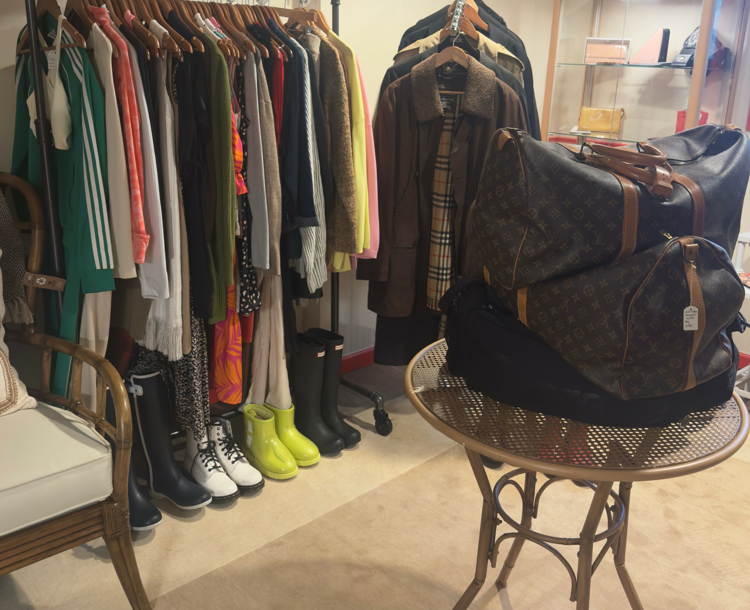 Clothing rack with colorful jackets and dresses, a table with bags, and chairs in a room.