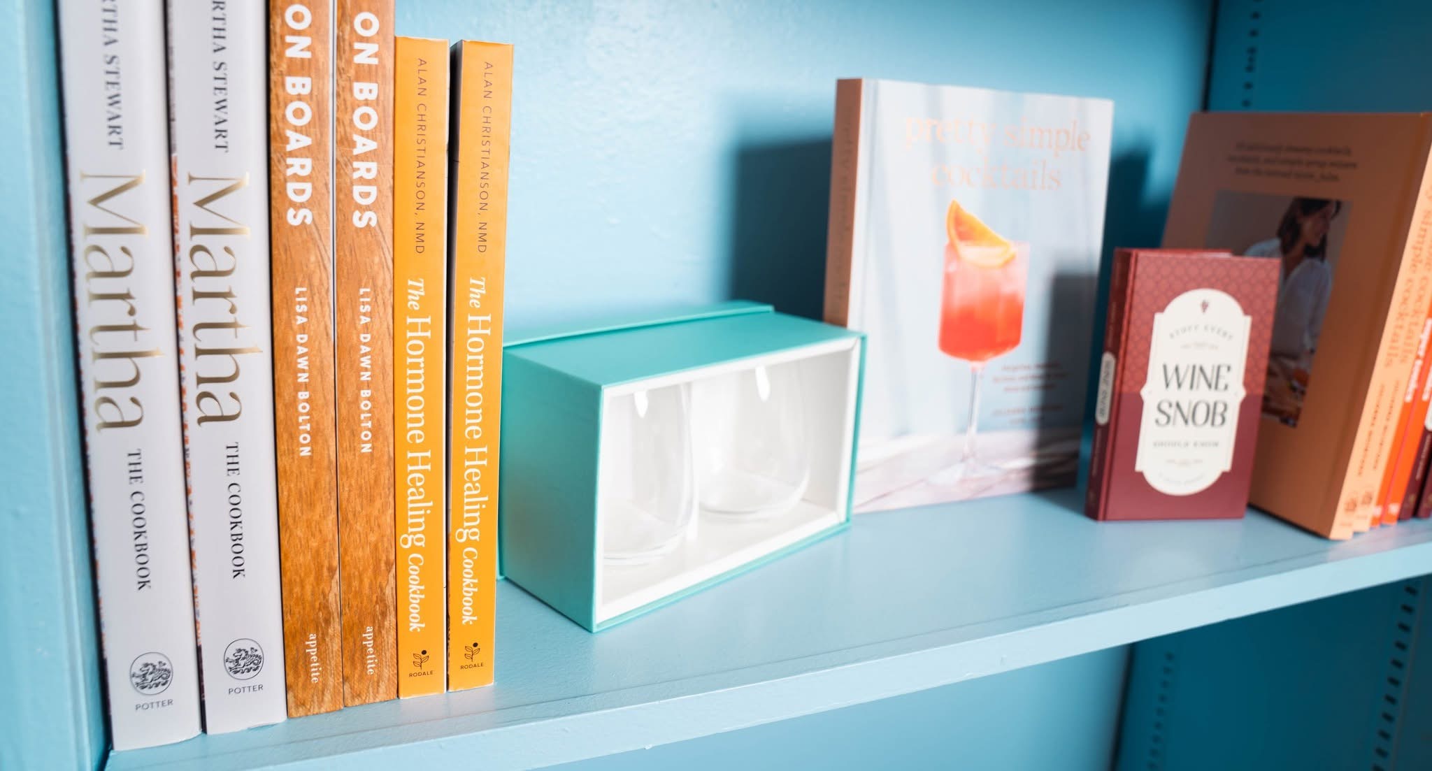 Books and a small box on a light blue shelf, with a teal wall in the background.