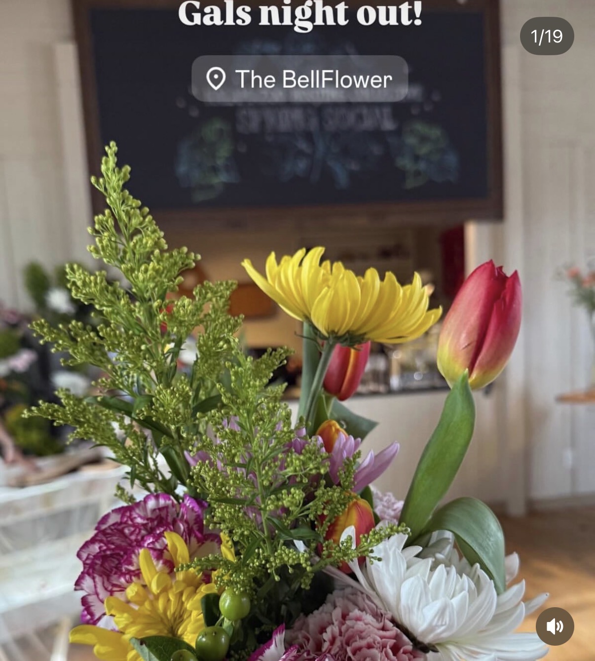 Colorful bouquet of flowers including yellow, pink, white, and purple blooms with green foliage, in front of a TV screen displaying event details.