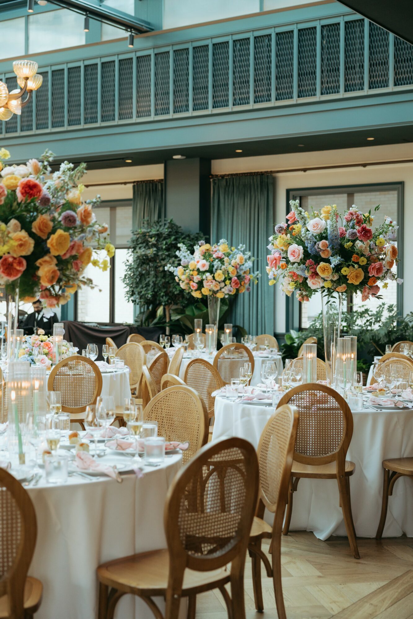 Elegant banquet hall with round tables, floral centerpieces, and chairs, set for a formal event with large windows and curtains.