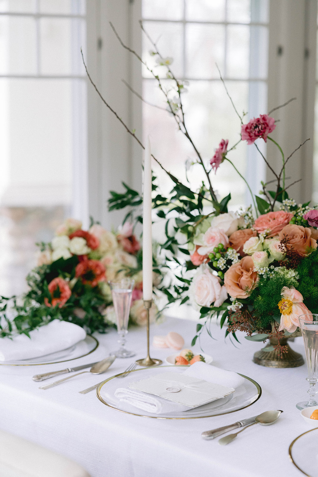 Elegant table setting with floral centerpiece, candles, and fine china, near a window with natural light.