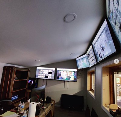Room with multiple monitors on the wall, a desk with a computer, and a window showing outside view.