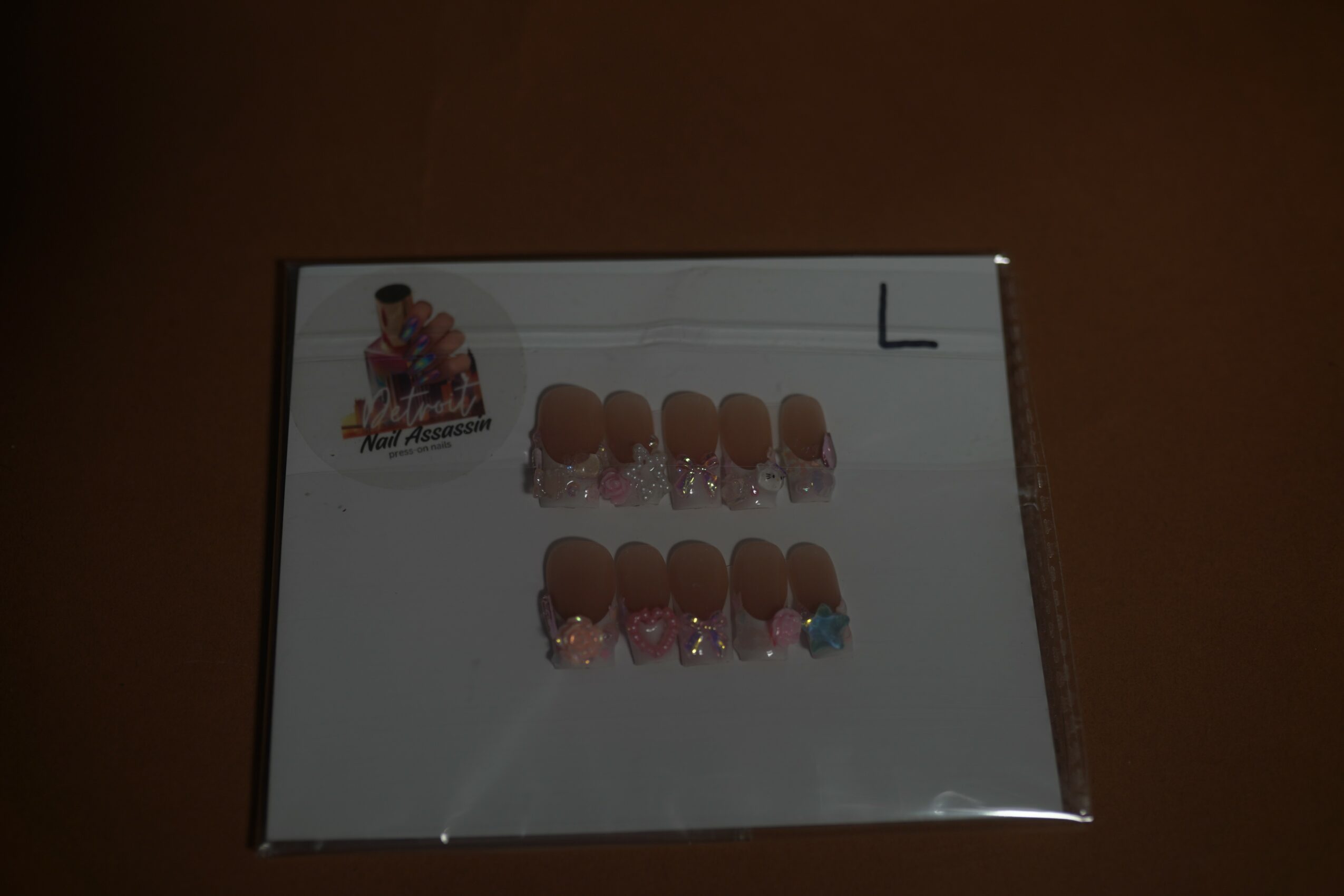 Box of false nails with pink and blue designs, labeled with letter L, on a white surface.