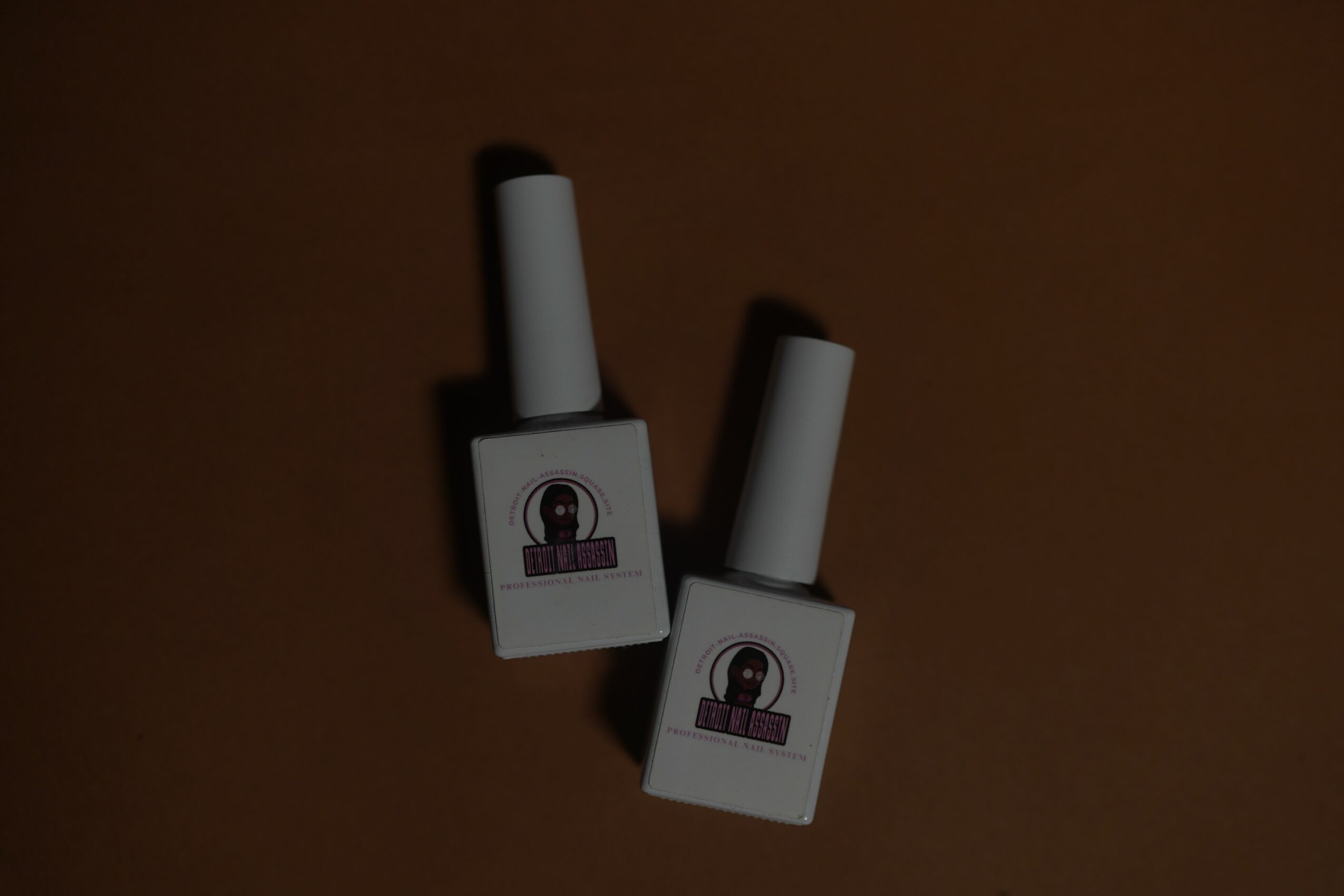 Two white nail polish bottles with black caps on a brown background.