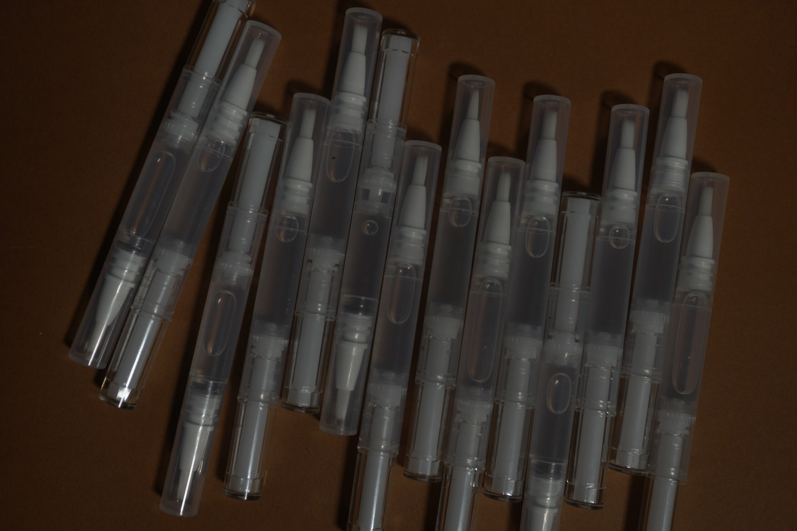 Multiple transparent spray pens arranged in a row on a dark surface.