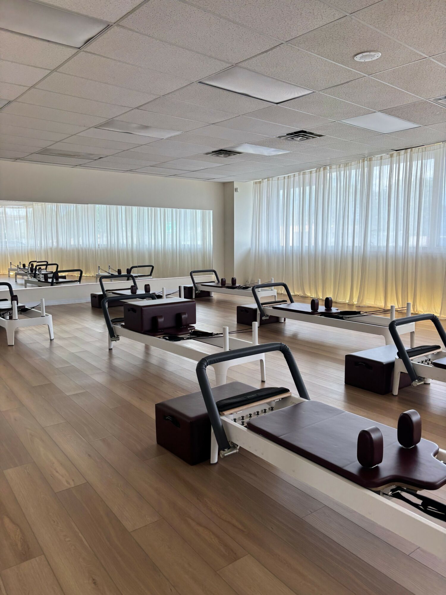 Gym with exercise equipment, wooden floor, and large windows with curtains.