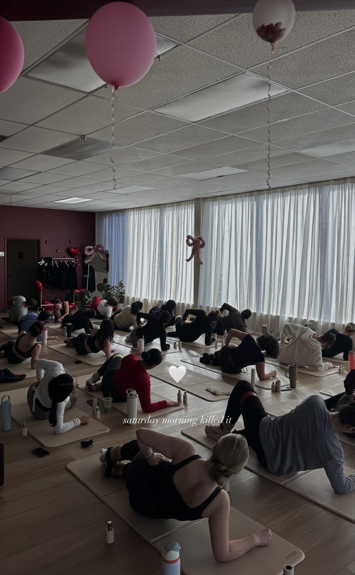 People practicing yoga or stretching on mats in a bright room with large windows and hanging decorations.