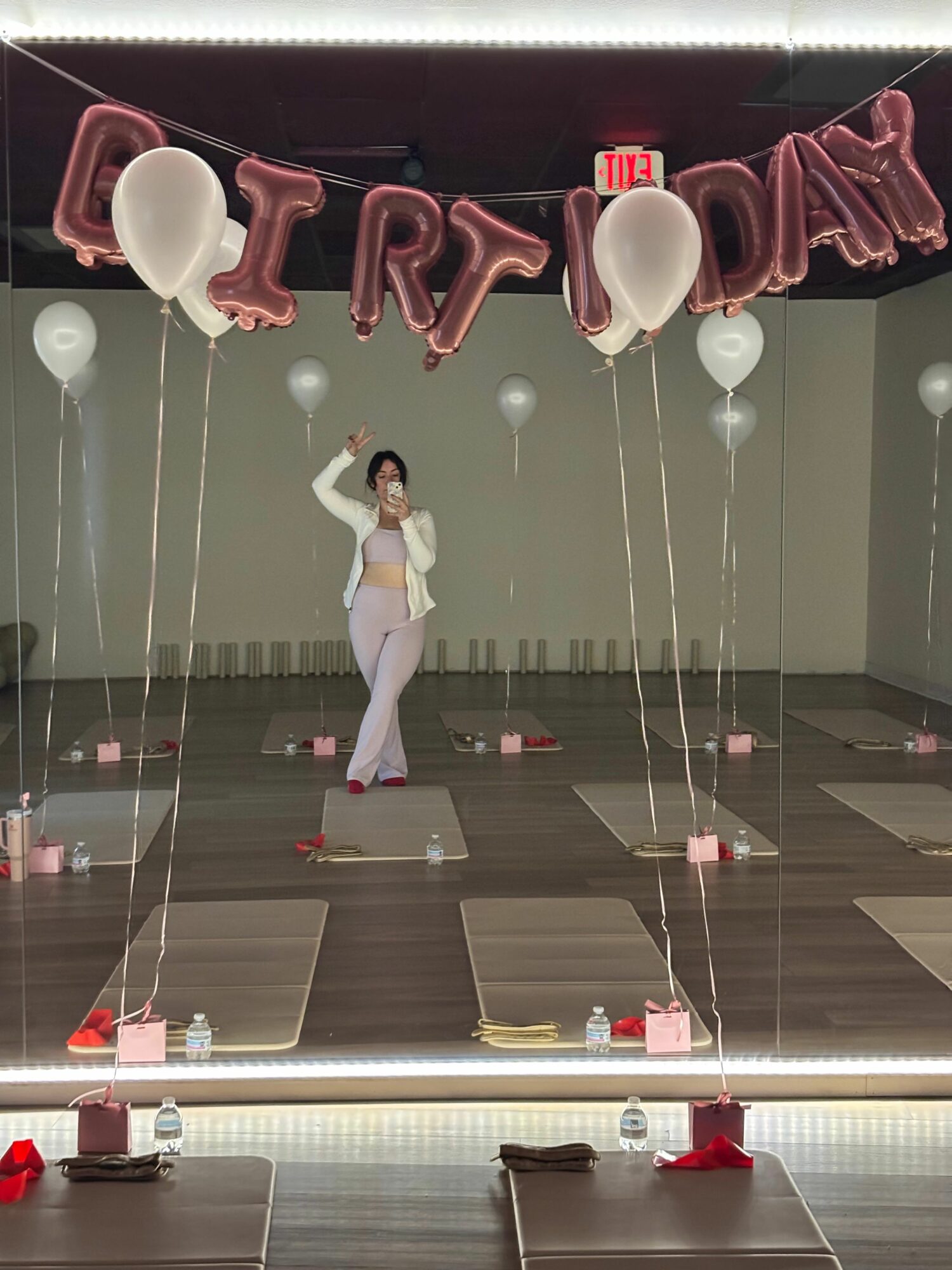 Person standing in a room with balloons spelling 'LOVE' and a mirror wall, with yoga mats on the floor.