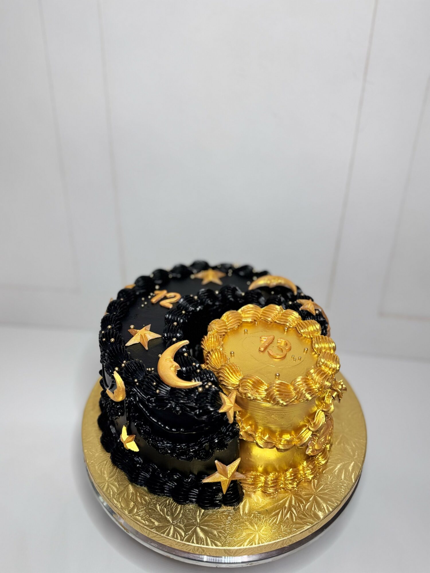 Decorative cake with black and gold celestial-themed decorations on a gold base, featuring stars, moons, and a gold coin-like element.