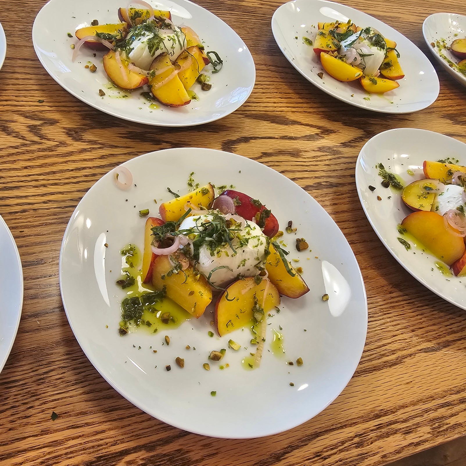 Four plates of food on a wooden table, each with sliced yellow and red vegetables, herbs, and sauce, arranged differently.