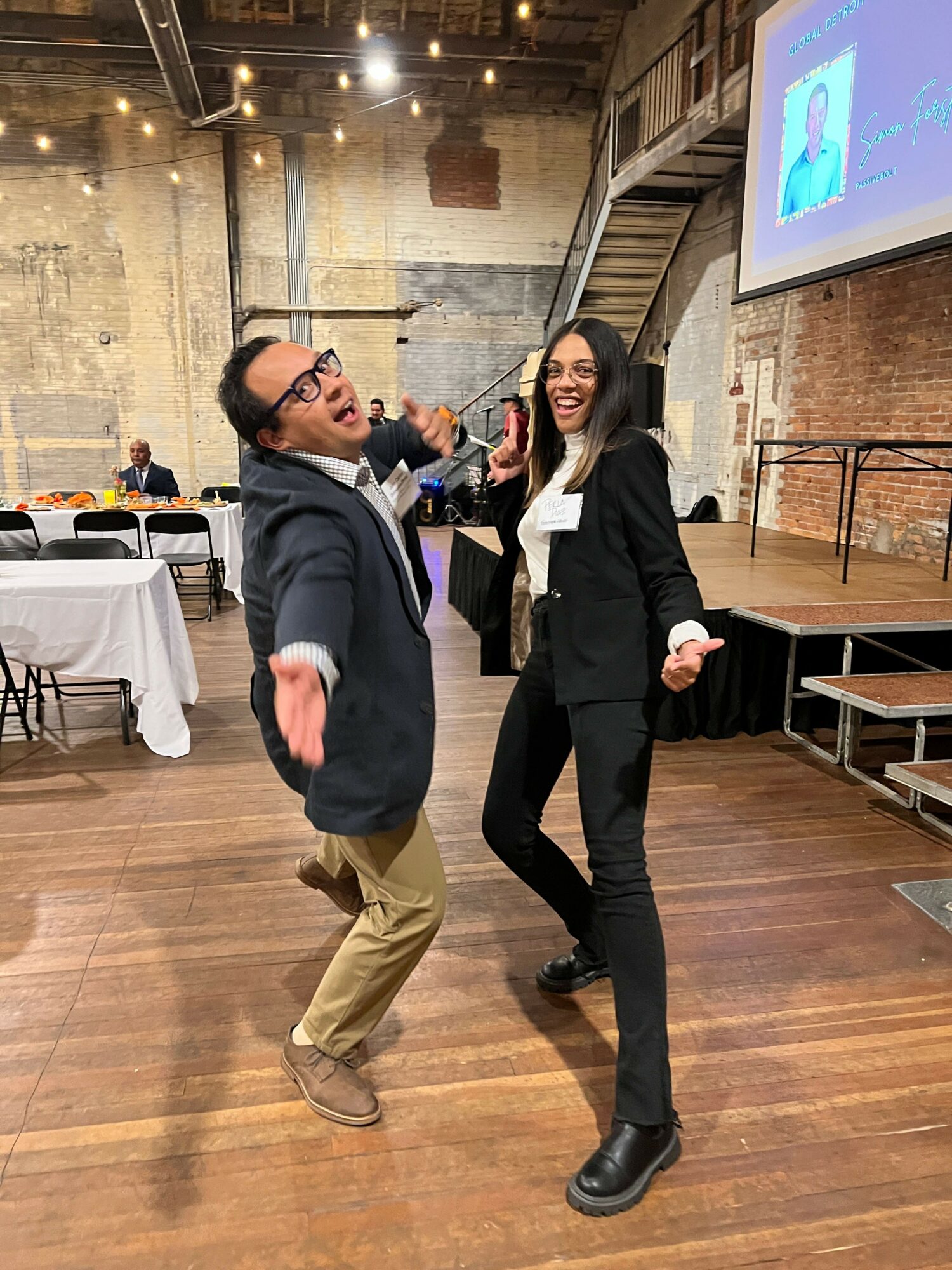Two people are standing and talking in a room with wooden floors and exposed brick walls.