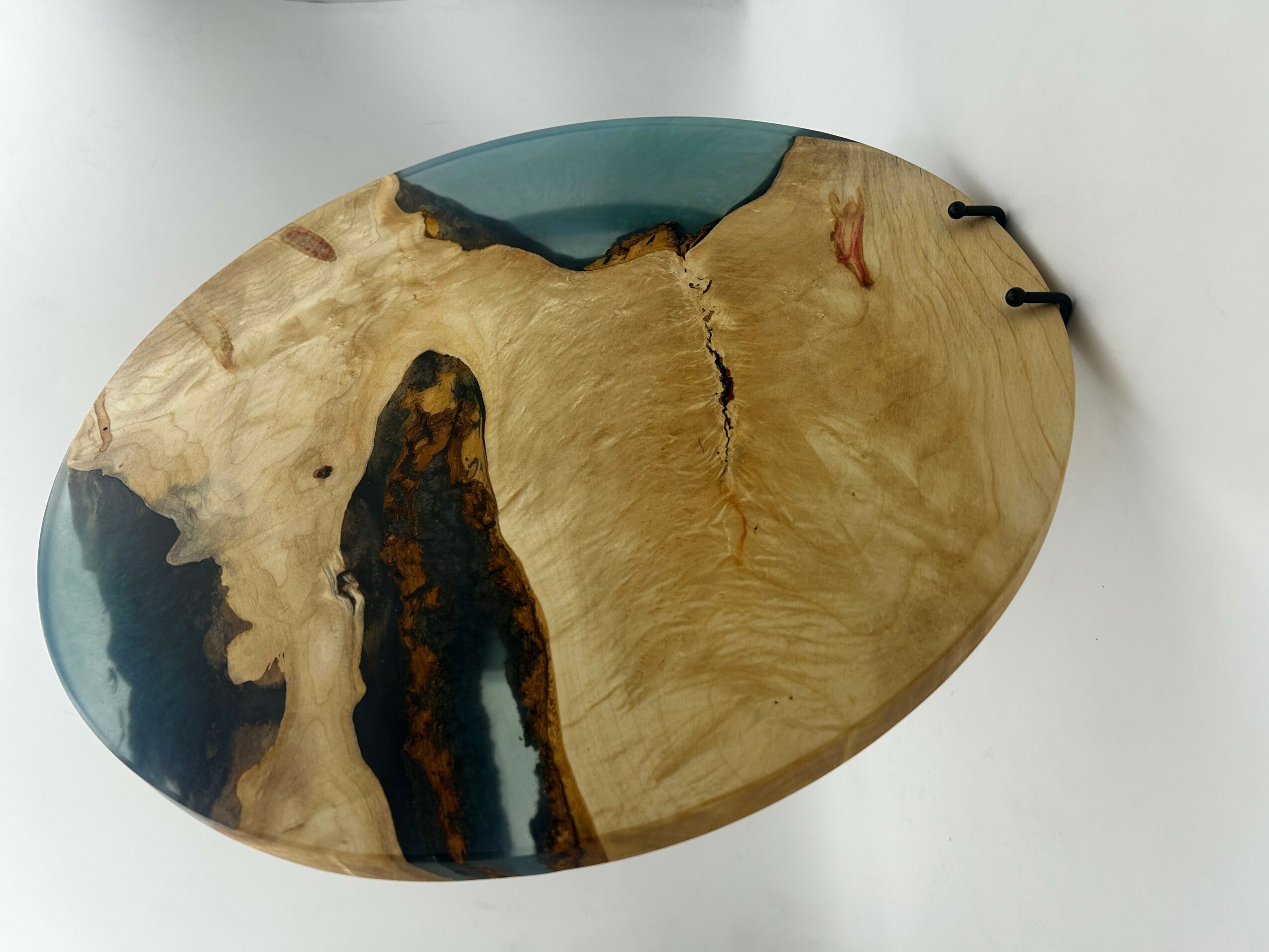 Wooden and resin art piece with natural wood grain and blue resin accents, oval shape, on a white background.