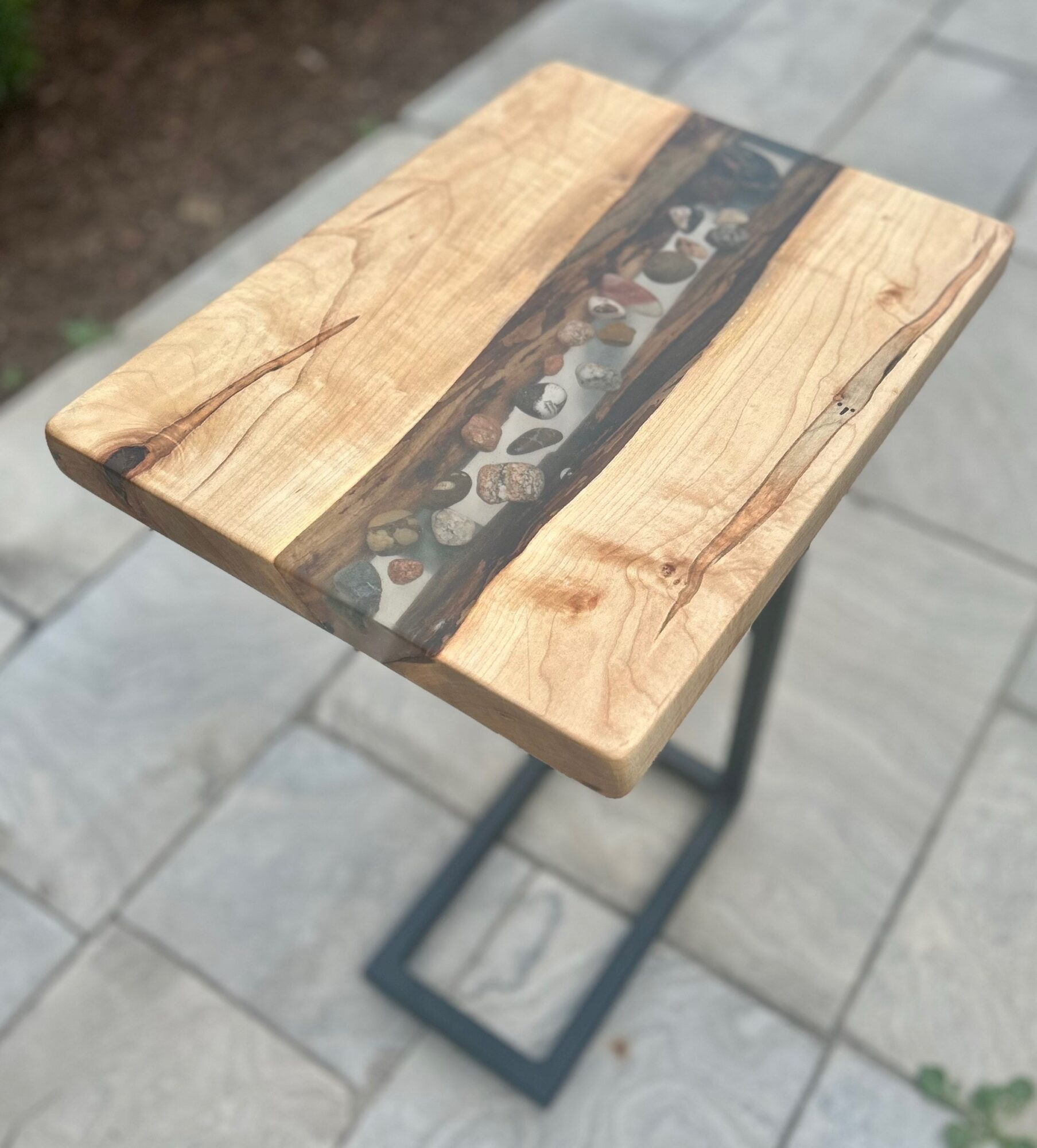 Wooden table with a decorative inlay, outdoors on a paved surface, with a metal frame, viewed from above.