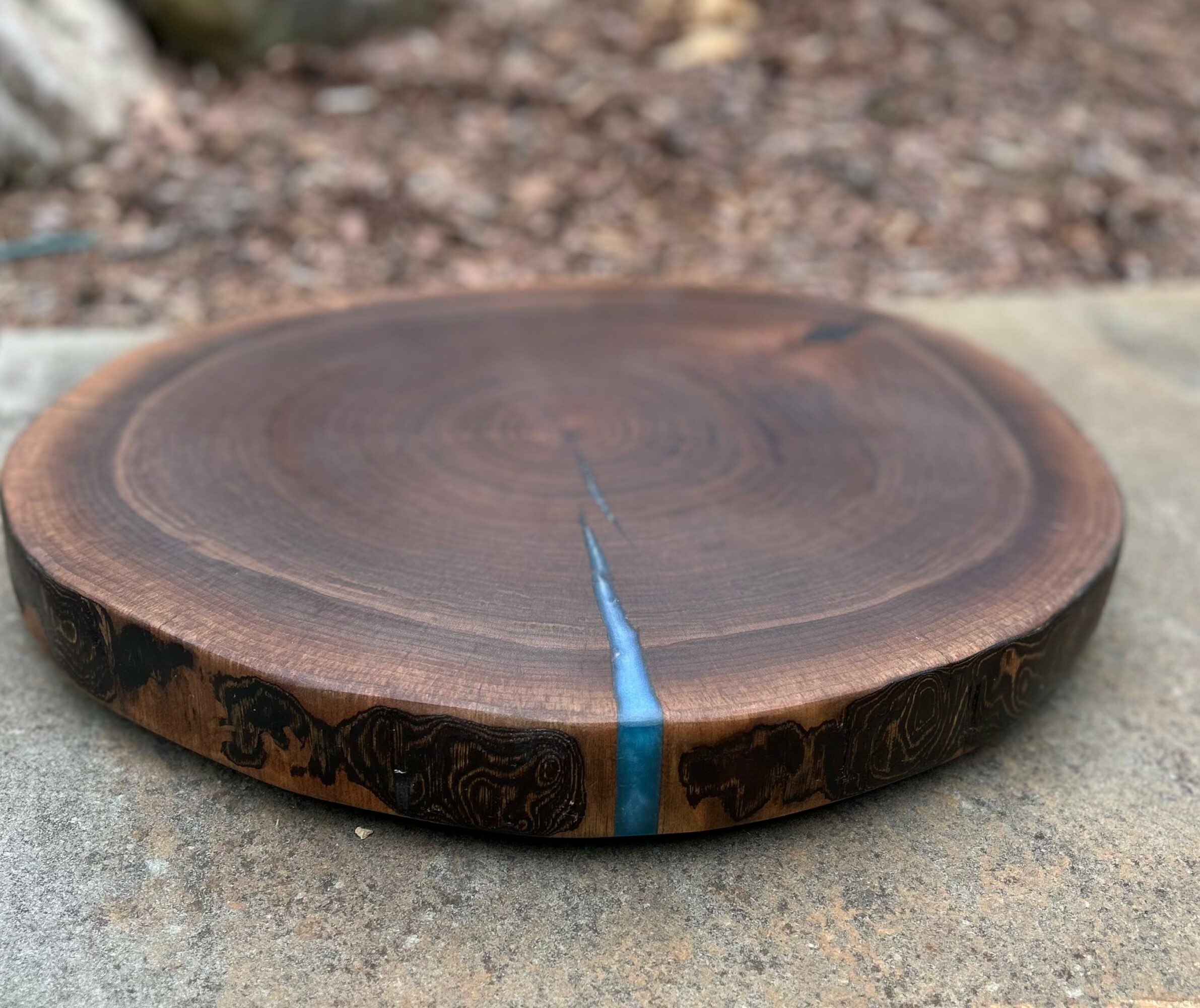 Round wooden slab with a blue crack, placed on a concrete surface outdoors.