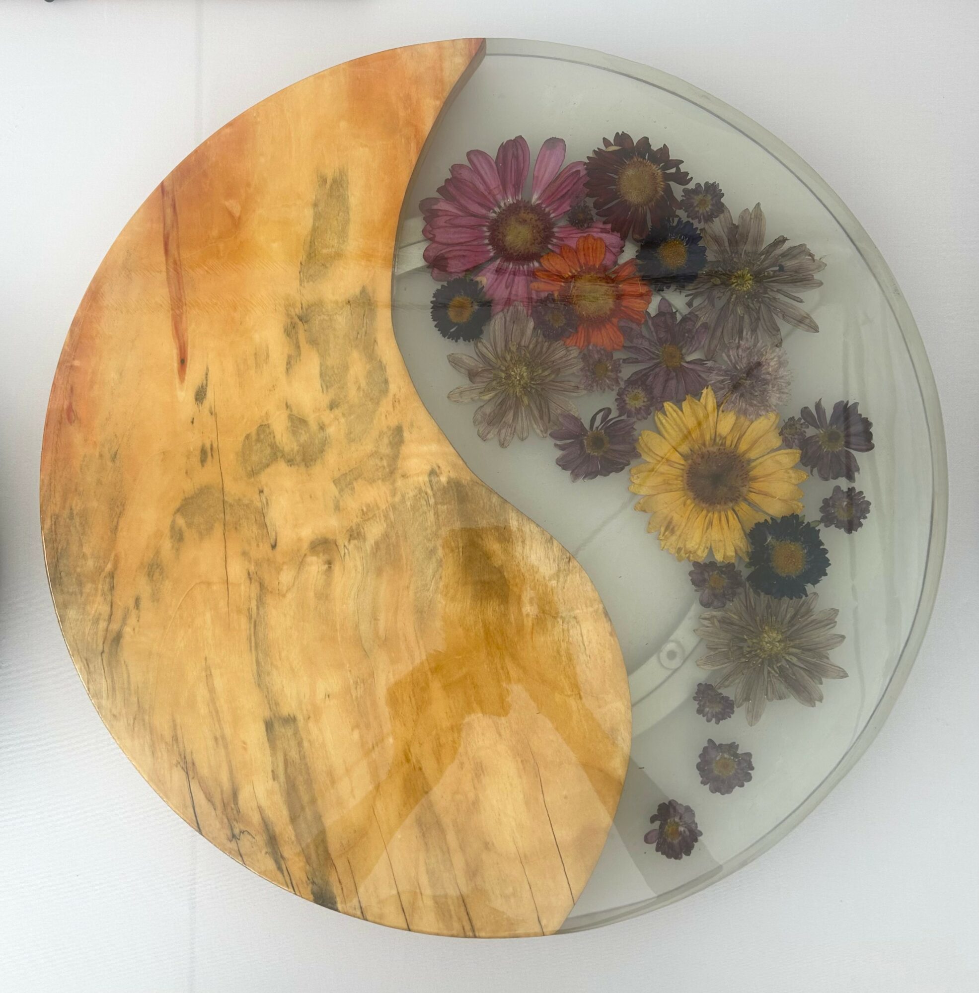 A circular glass table with dried flowers inside, partially covered by a wooden semi-circle, viewed from above.
