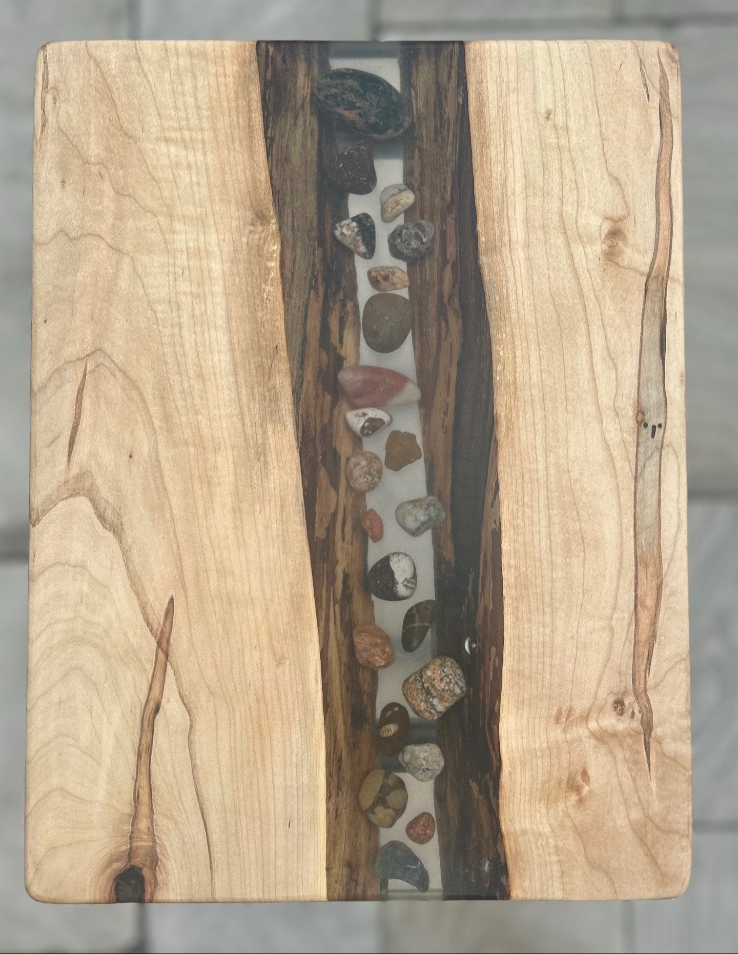 Wooden surface with a vertical strip of small stones embedded in the center, surrounded by light-colored wood.
